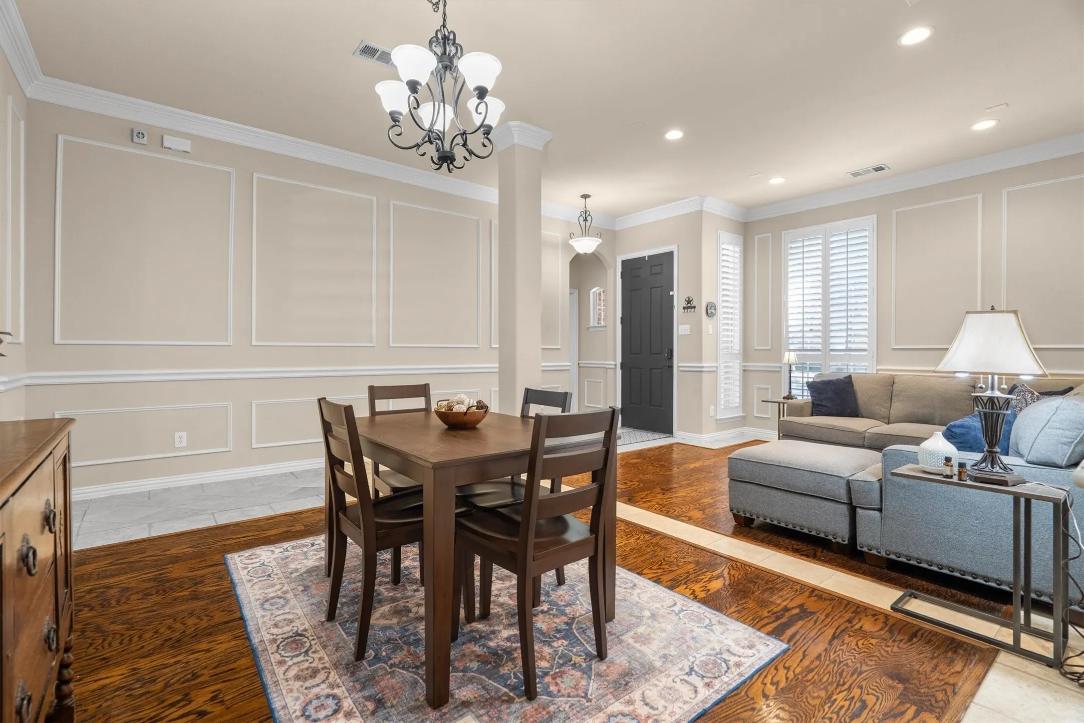 Wainscoting and crown molding details, recessed lighting, wood-finish flooring, plantation shutters, and a dark-paneled entry door