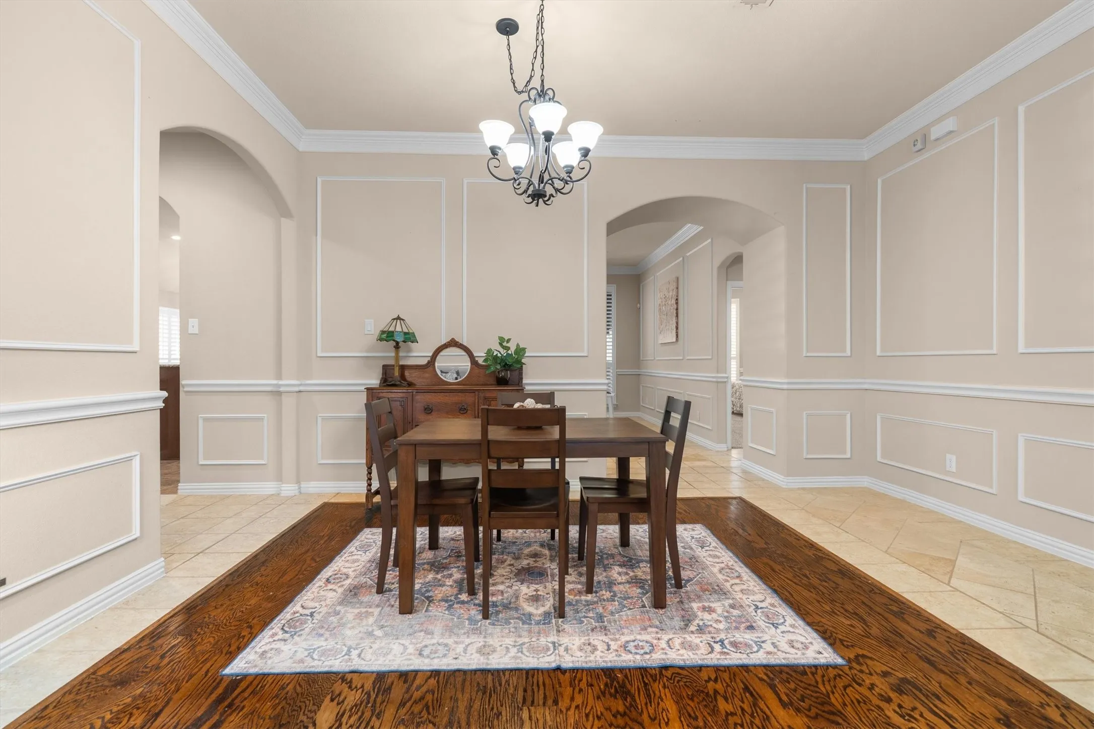 Arched doorways with decorative trim, extensive crown molding, chair rail, and picture frame molding on walls, wood-finish flooring, and a chandelier