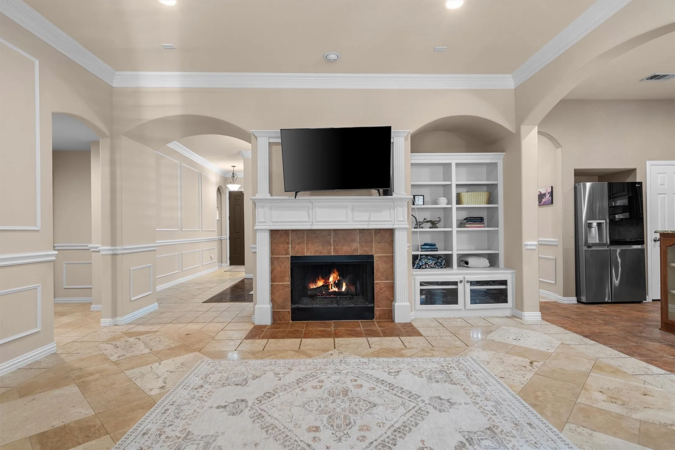 Tiled flooring with contrasting patterns, fireplace with a tiled surround, white mantel, built-in shelving, and crown molding