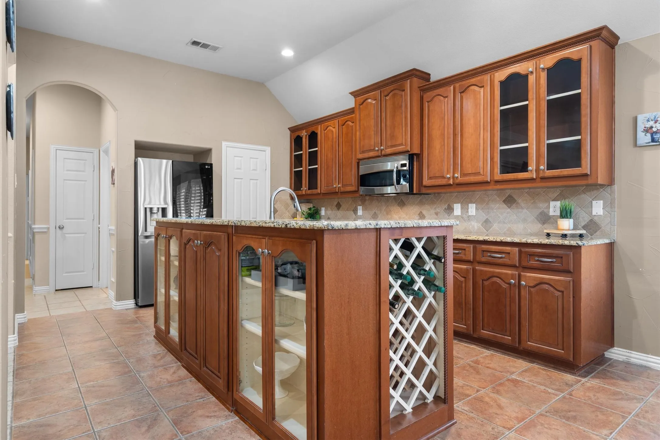 Kitchen featuring an expansive island with built-in wine storage and glass-front cabinetry, granite countertops, and a full tile backsplash