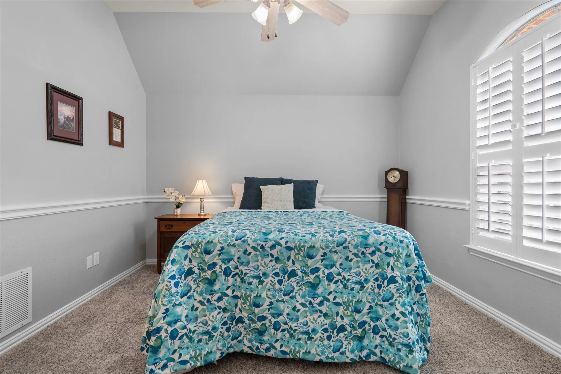 Vaulted ceiling, ceiling fan, carpet flooring, decorative wall molding, and arched window with plantation shutters