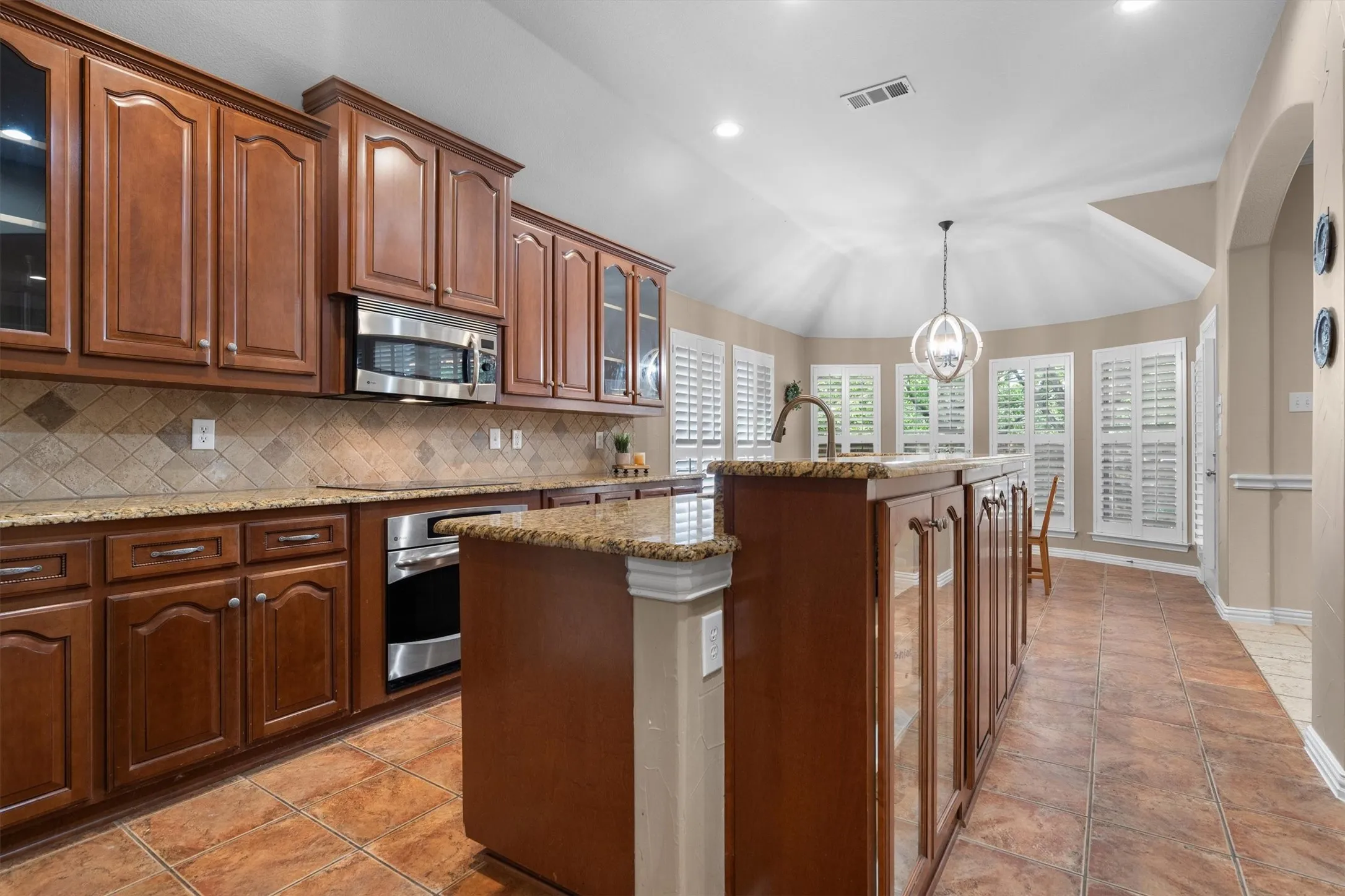 Kitchen featuring wood cabinetry, stainless steel appliances, granite countertops, and tile flooring