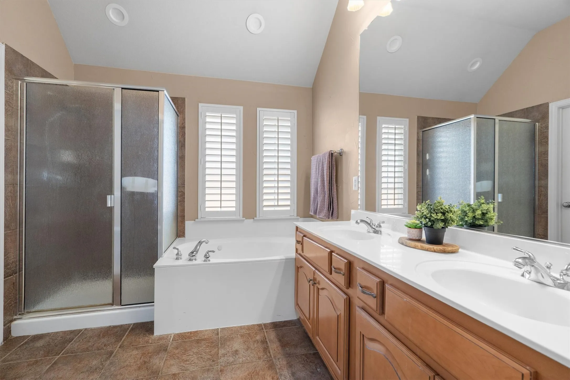 Spacious bathroom featuring a dual vanity with integrated sinks, a built-in soaking tub, a glass-enclosed shower, and plantation shutters