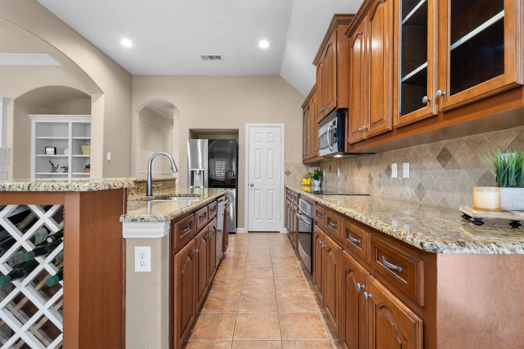Kitchen featuring extensive cabinetry, integrated stainless steel appliances, a center island with a built-in wine rack, and tile flooring