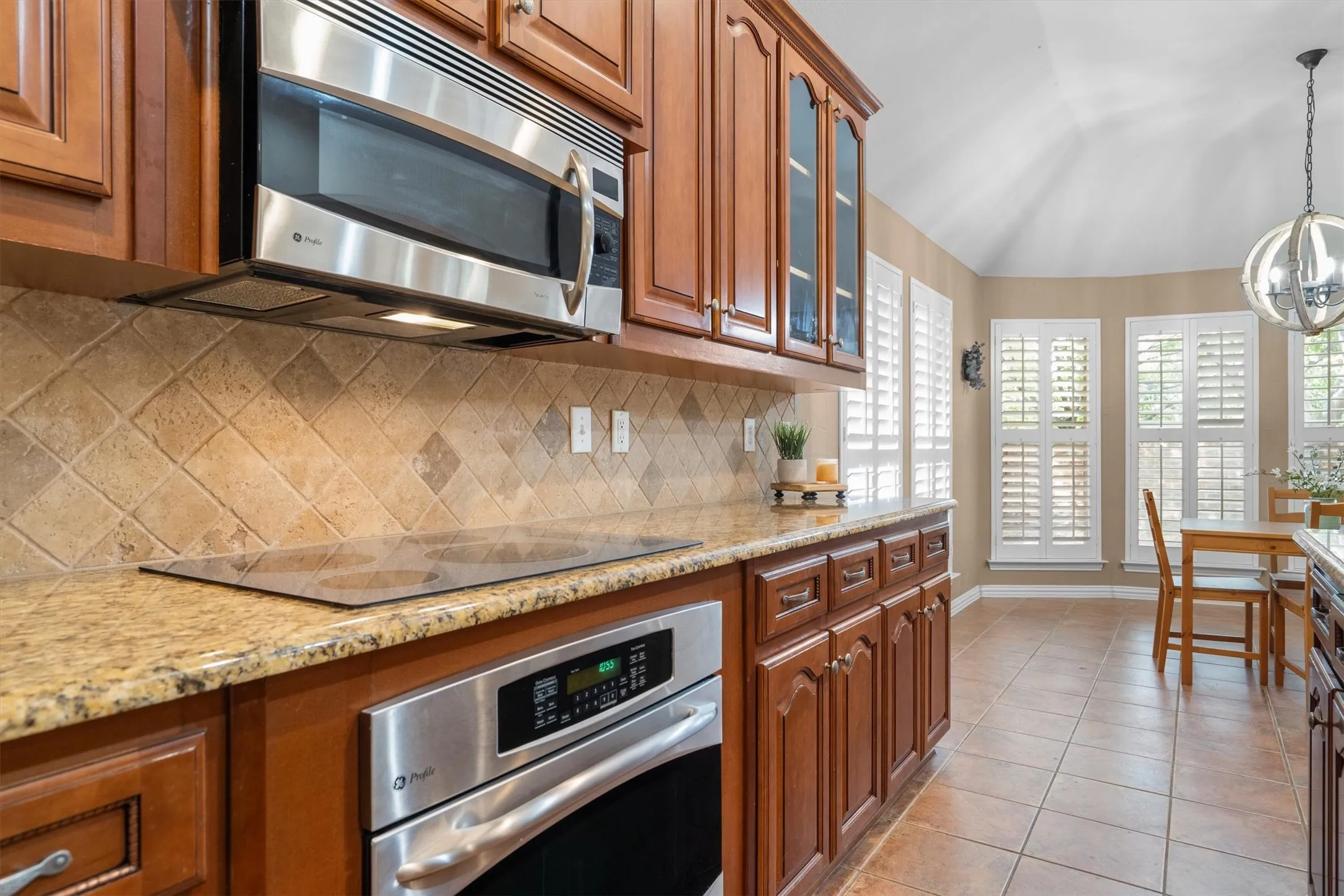 Wood-finish cabinetry with glass-front accents, stainless steel appliances, granite countertops, and a tile backsplash