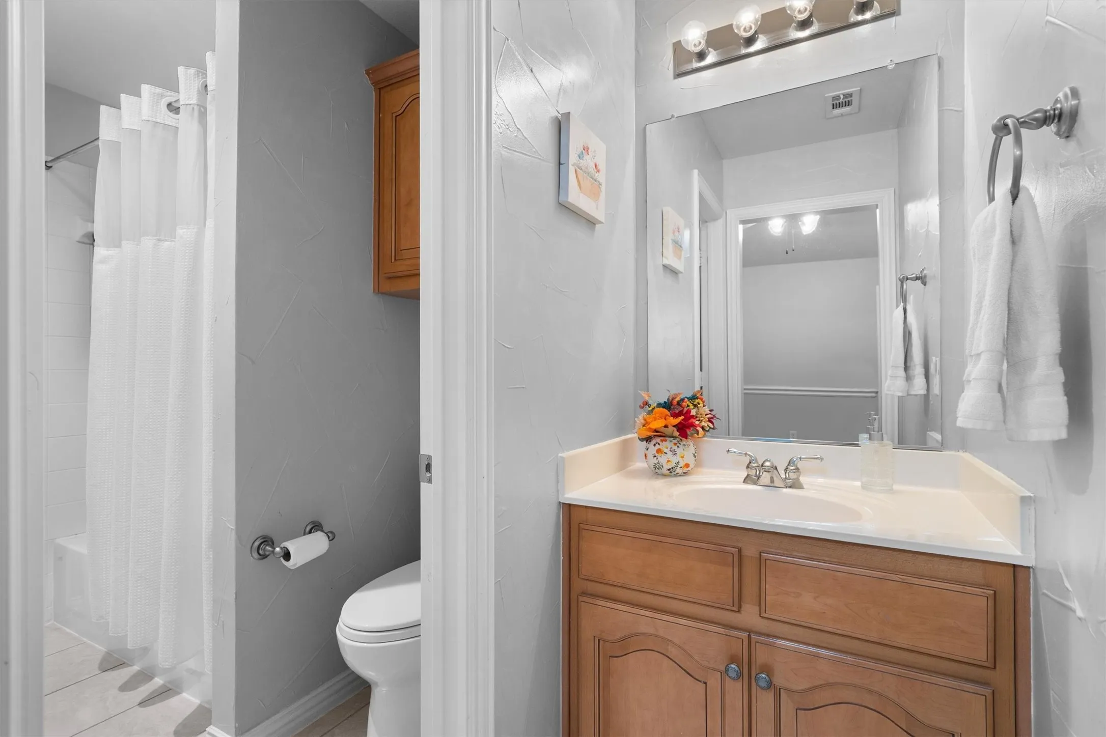 Bathroom featuring a single vanity with wood-finish cabinetry, a ceramic sink, a polished chrome faucet, and a wall-mounted mirror with overhead lighting