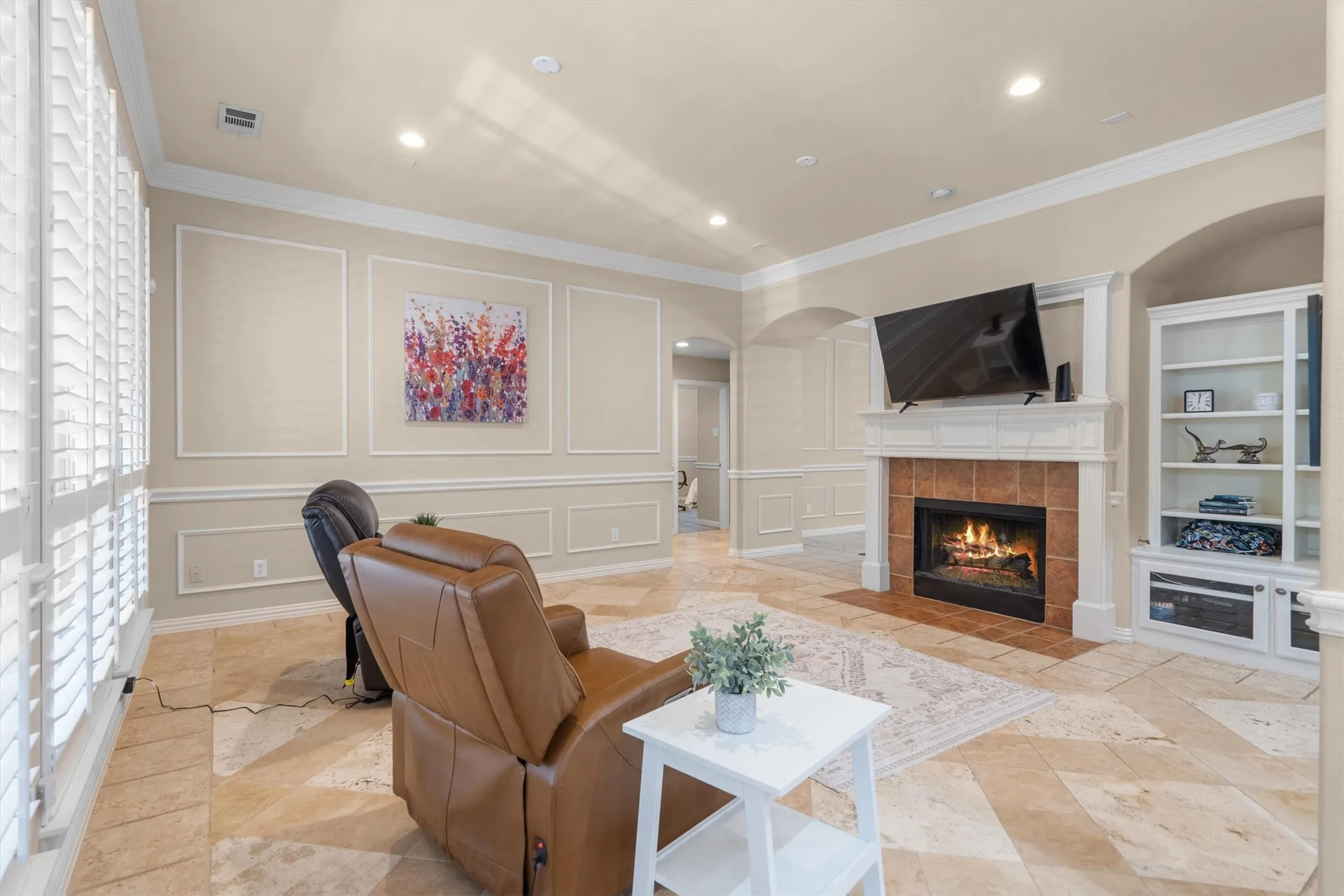 Stone tile flooring, decorative wall molding, built-in fireplace with tile surround and mantel, built-in shelving, and plantation shutters