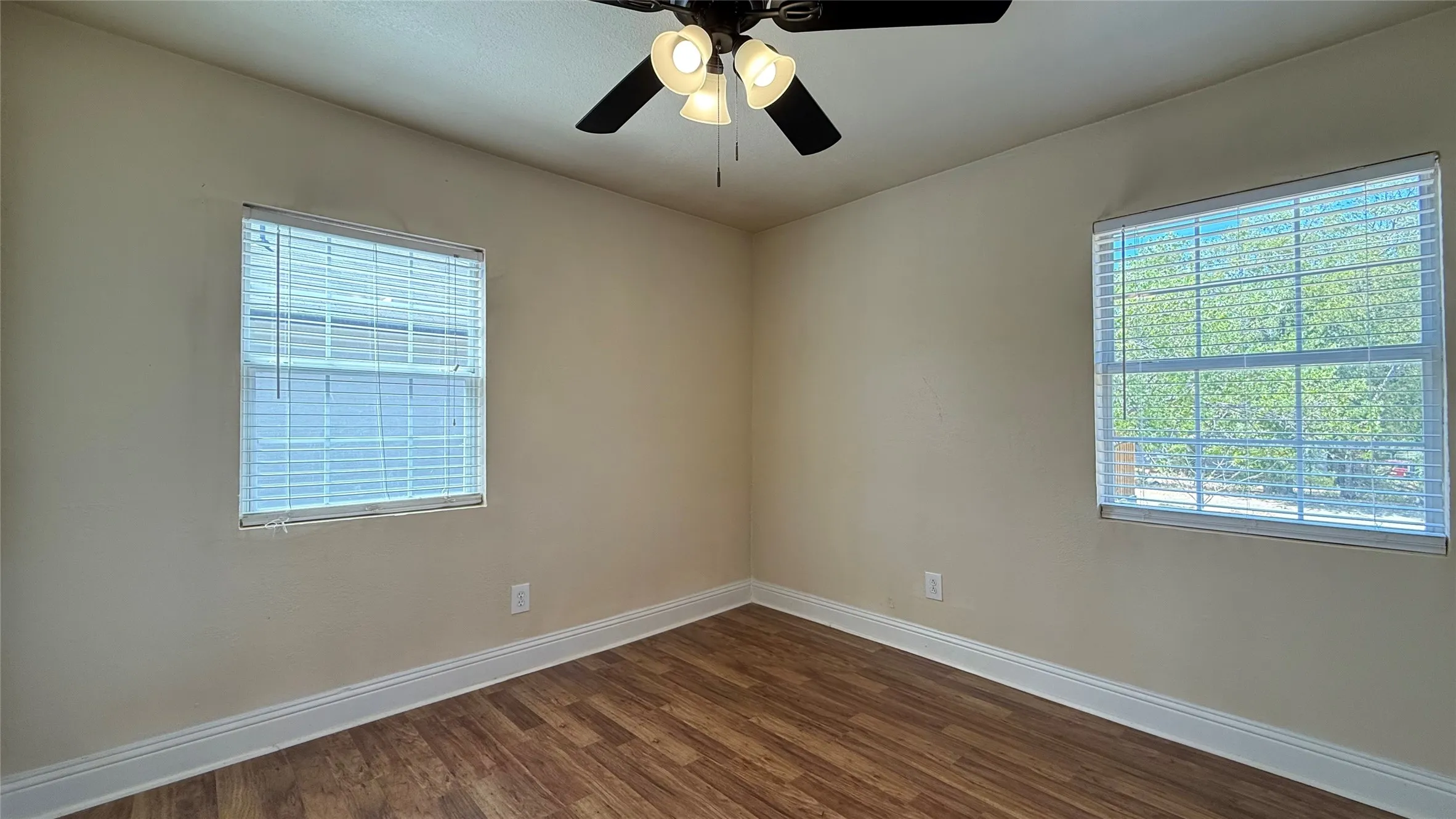 Wood-finish flooring, two windows with blinds, ceiling fan with light fixture, and neutral wall tones