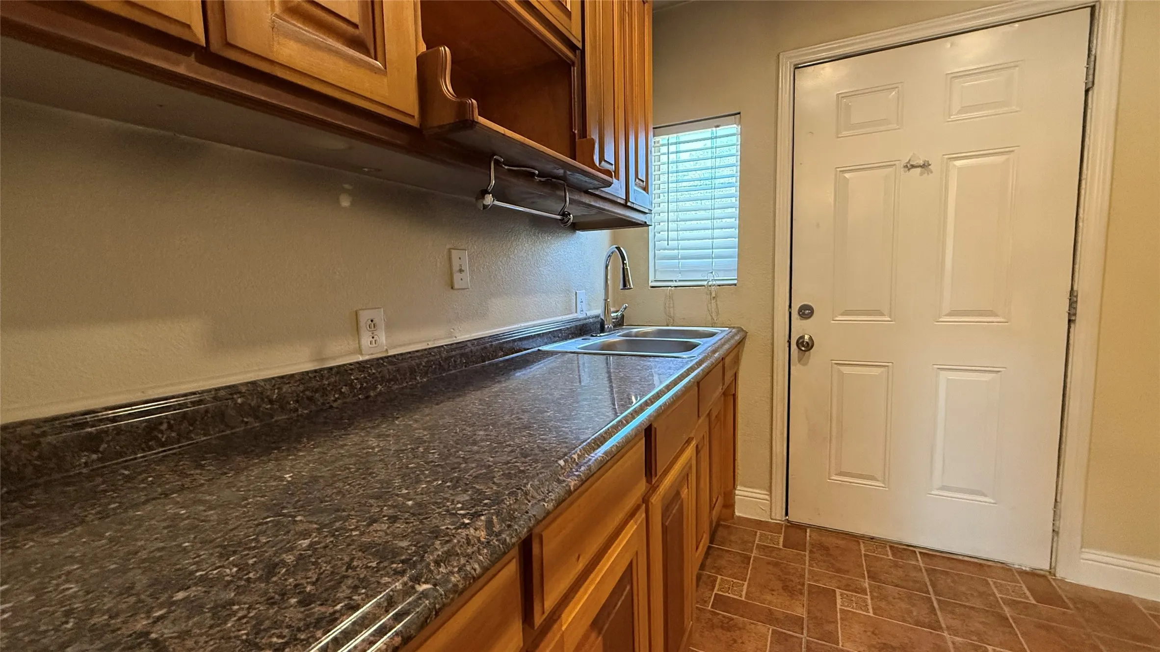 Wood-finish cabinetry with a built-in shelf, double basin stainless steel sink, contemporary faucet, and a patterned countertop