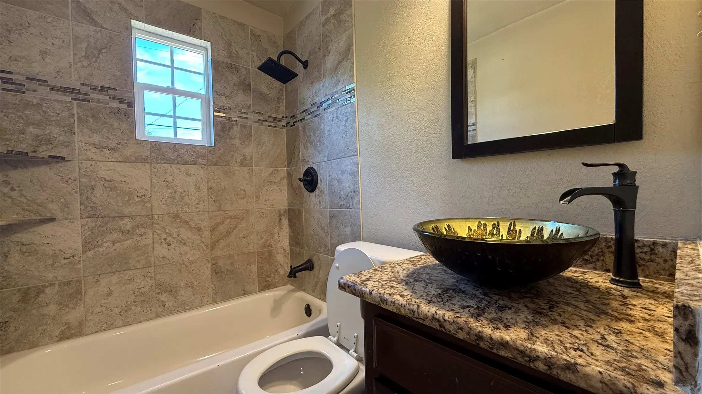 Bathtub and shower combination featuring neutral-toned wall tiling with decorative accent band, dark bronze shower head, and matching fixtures