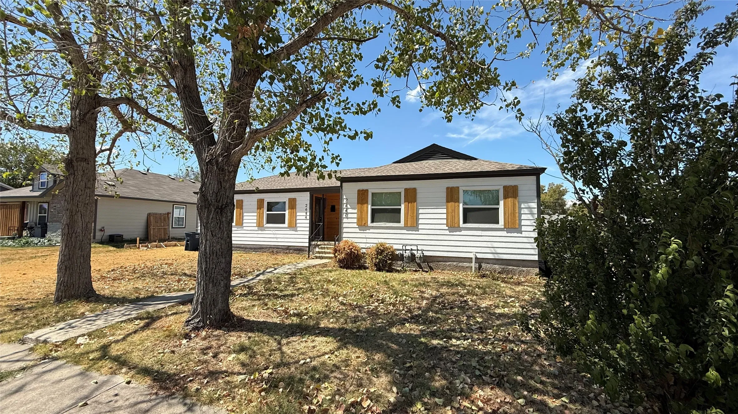 White siding exterior with natural wood-finish shutters, dark roof, and mature trees