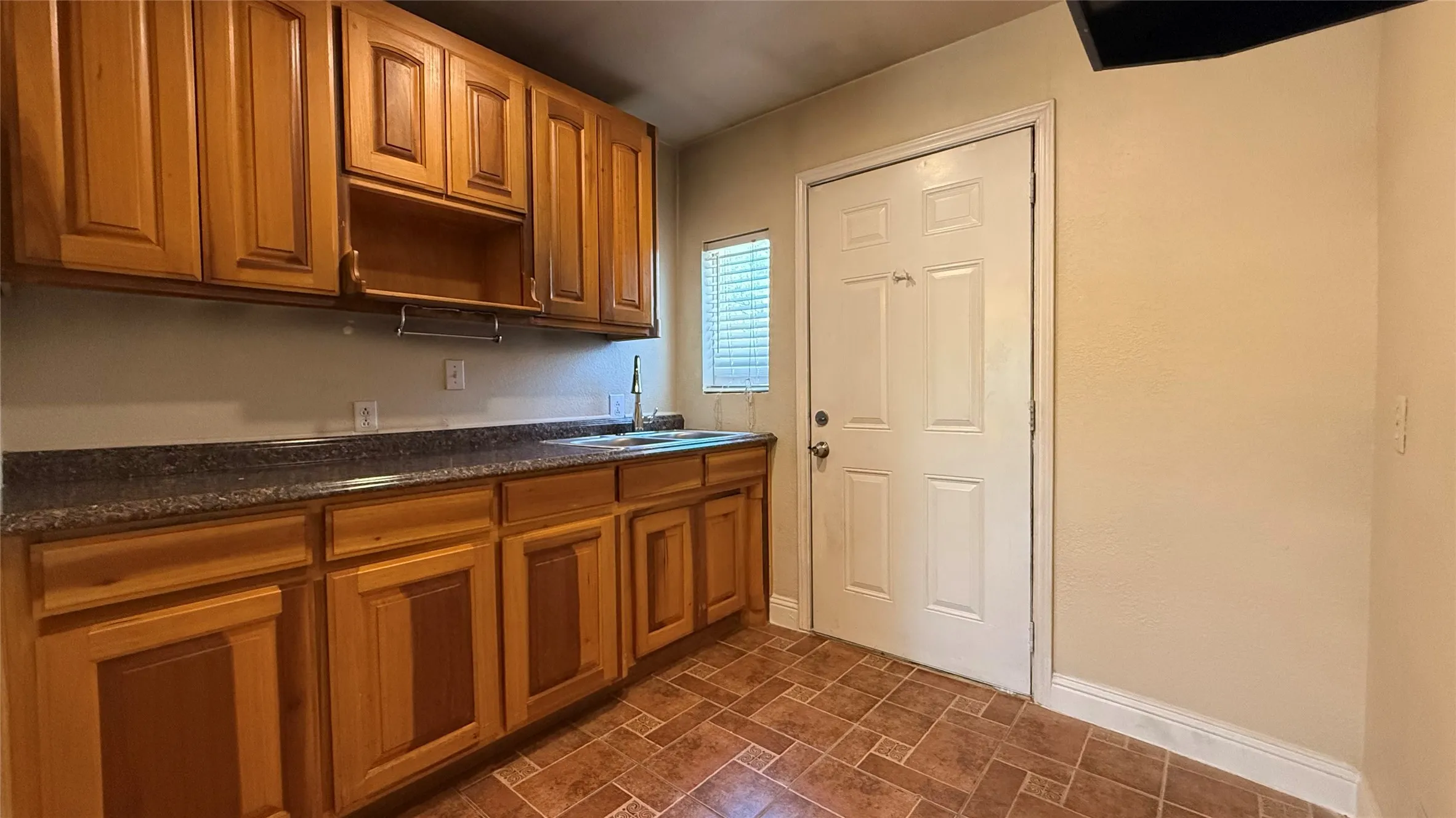 Wood-finish cabinetry with dark countertops, a stainless steel sink, and a white paneled door