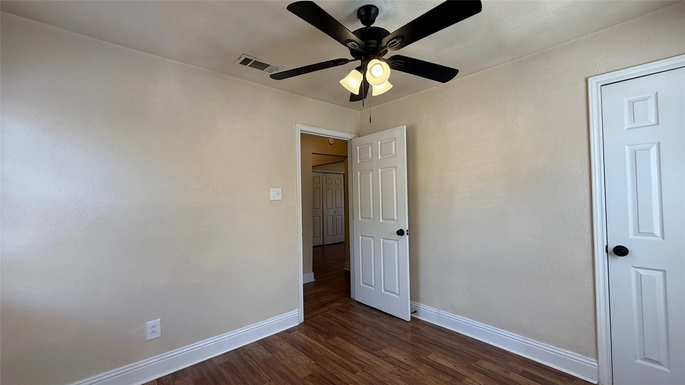 Wood-finish flooring with white baseboards, a ceiling fan with light fixture, and neutral wall tones