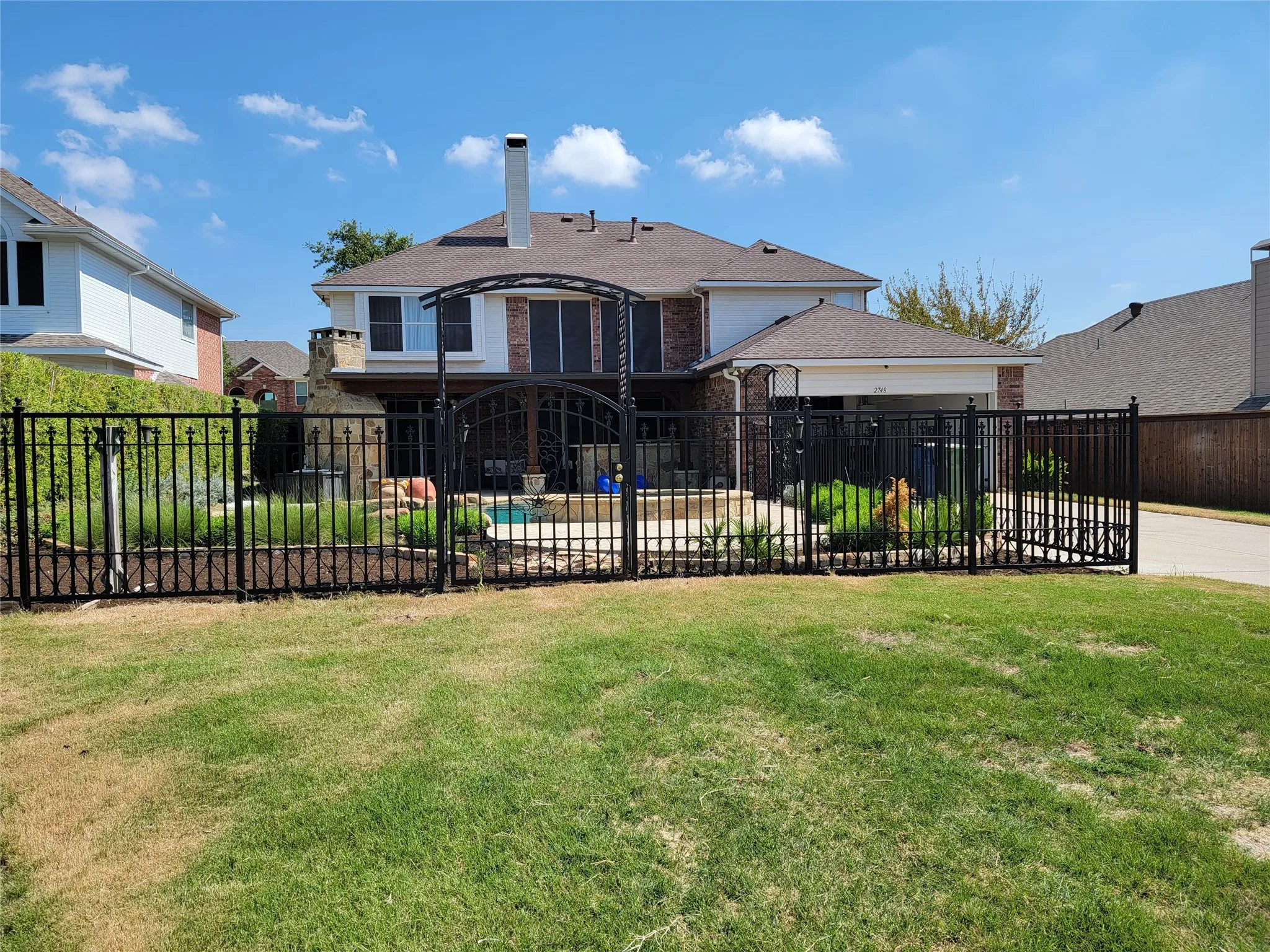 Wrought iron fencing with ornate gate, brick and siding exterior, multi-story structure, outdoor living space, and a swimming pool