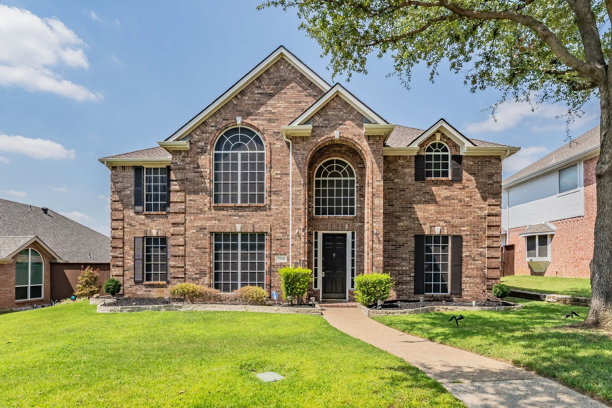 Brick facade residence featuring multiple gables, arched windows, and a concrete pathway leading to the front entry