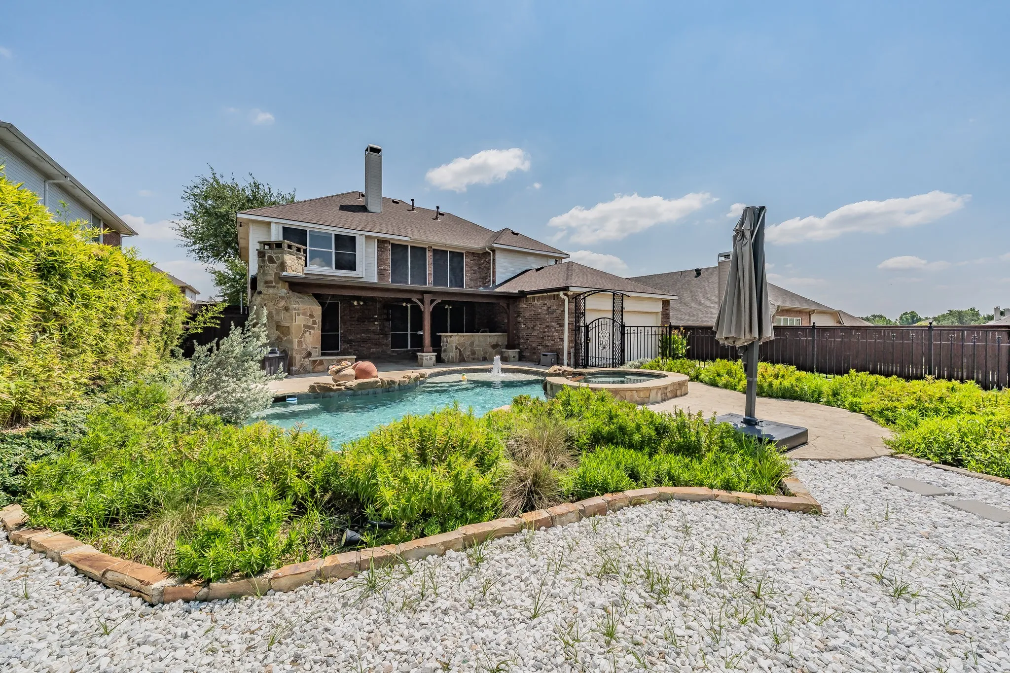 Curved-edge swimming pool with hot tub, complemented by a stone-clad outdoor fireplace and an expansive covered patio
