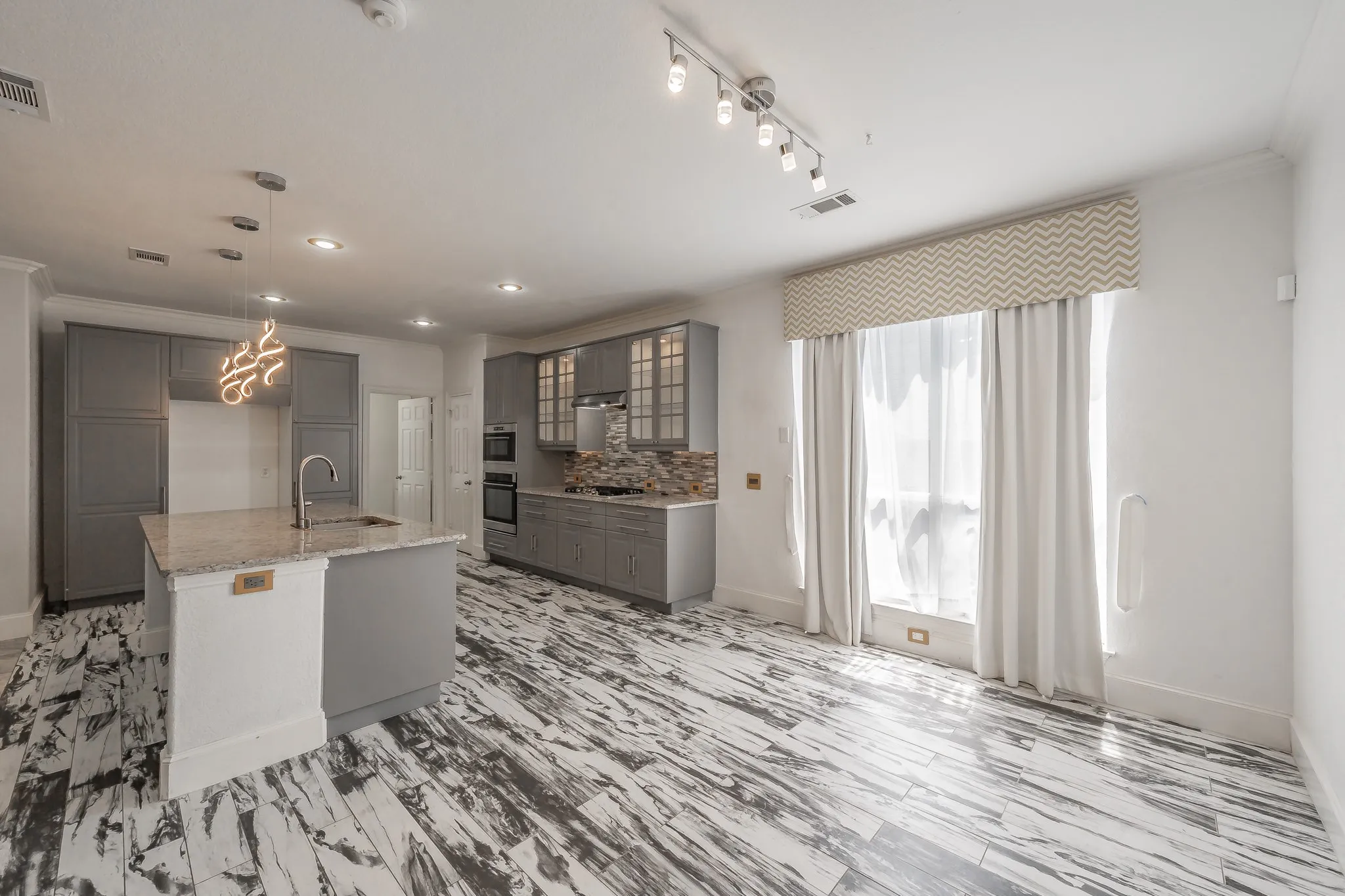 Kitchen featuring gray cabinets, hanging light fixtures, glass insert cabinets, decorative backsplash, and ornamental molding