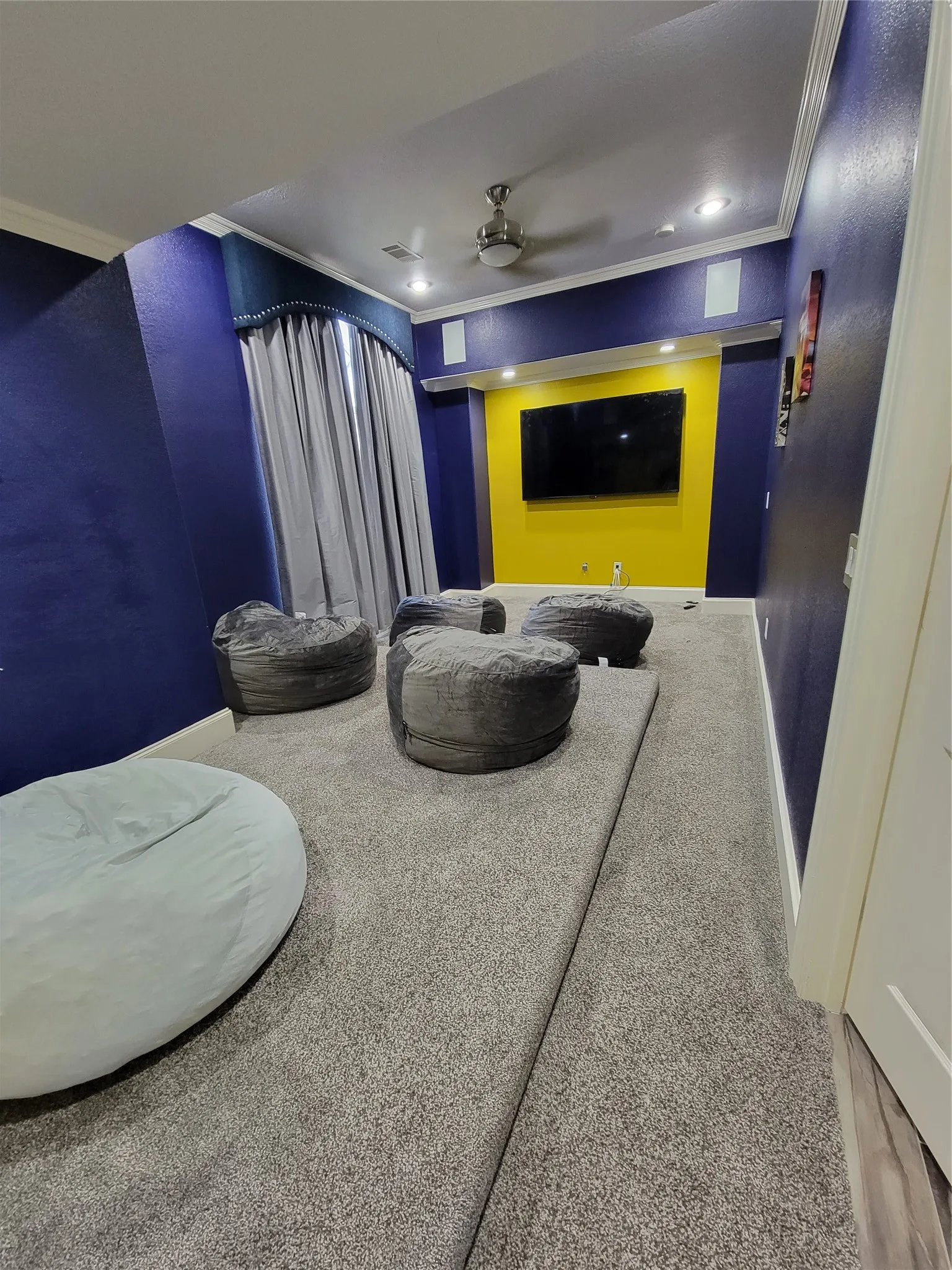 Recessed lighting, ceiling fan, crown molding, wall-mounted display, and an elevated carpeted platform