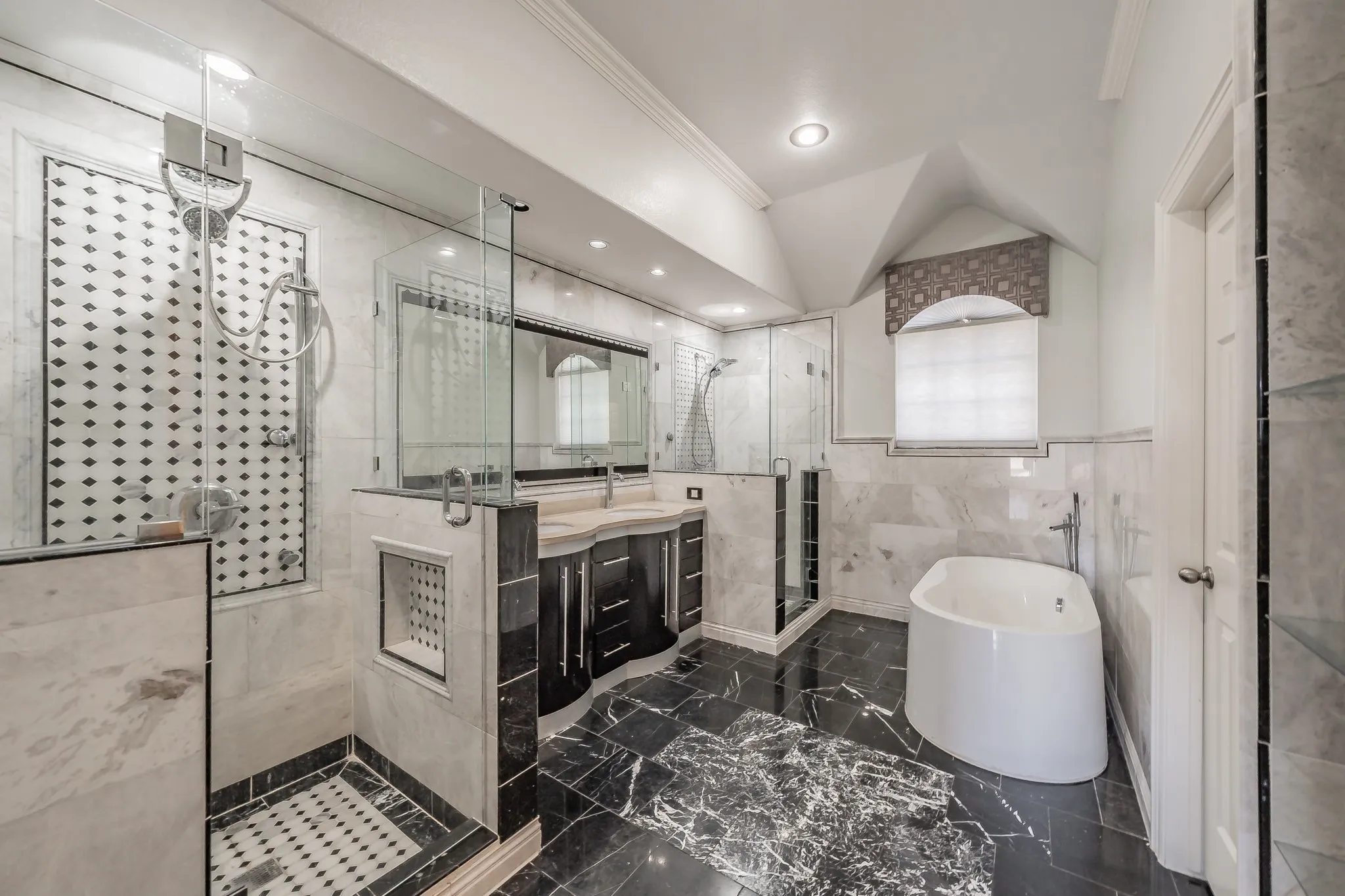Dual glass-enclosed showers, freestanding soaking tub, dual vanity with undermount sinks, recessed lighting, and black stone flooring