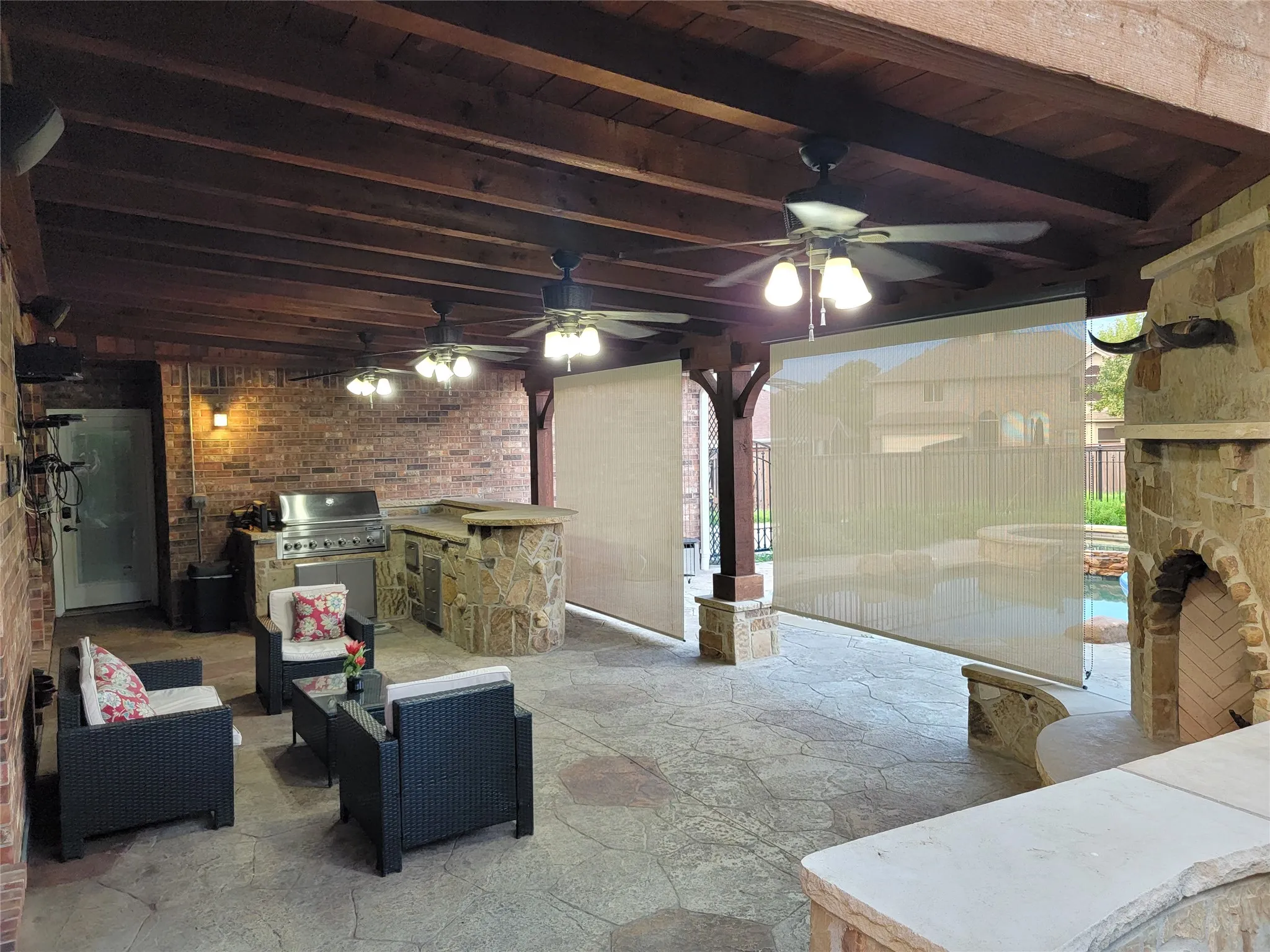 Expansive covered patio with a wood-beamed ceiling, multiple ceiling fans, and an outdoor kitchen featuring a built-in grill