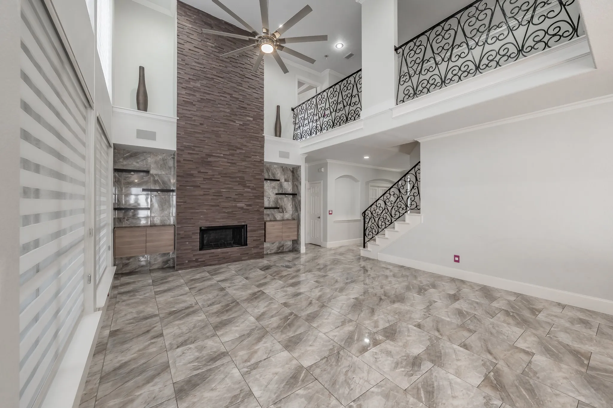 Two-story living area featuring a stone accent wall with an integrated fireplace, tile flooring, and a decorative wrought iron staircase
