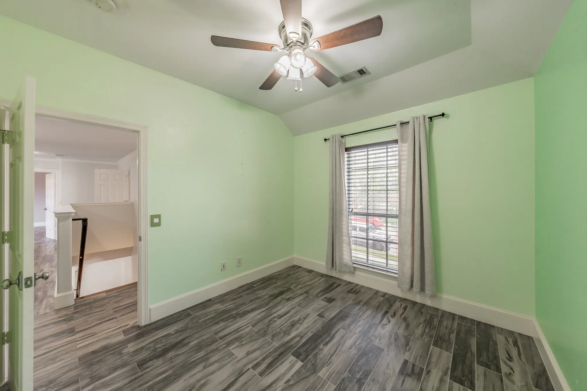 Vaulted ceiling featuring a ceiling fan with light fixture, wood-look laminate flooring, and a window with blinds