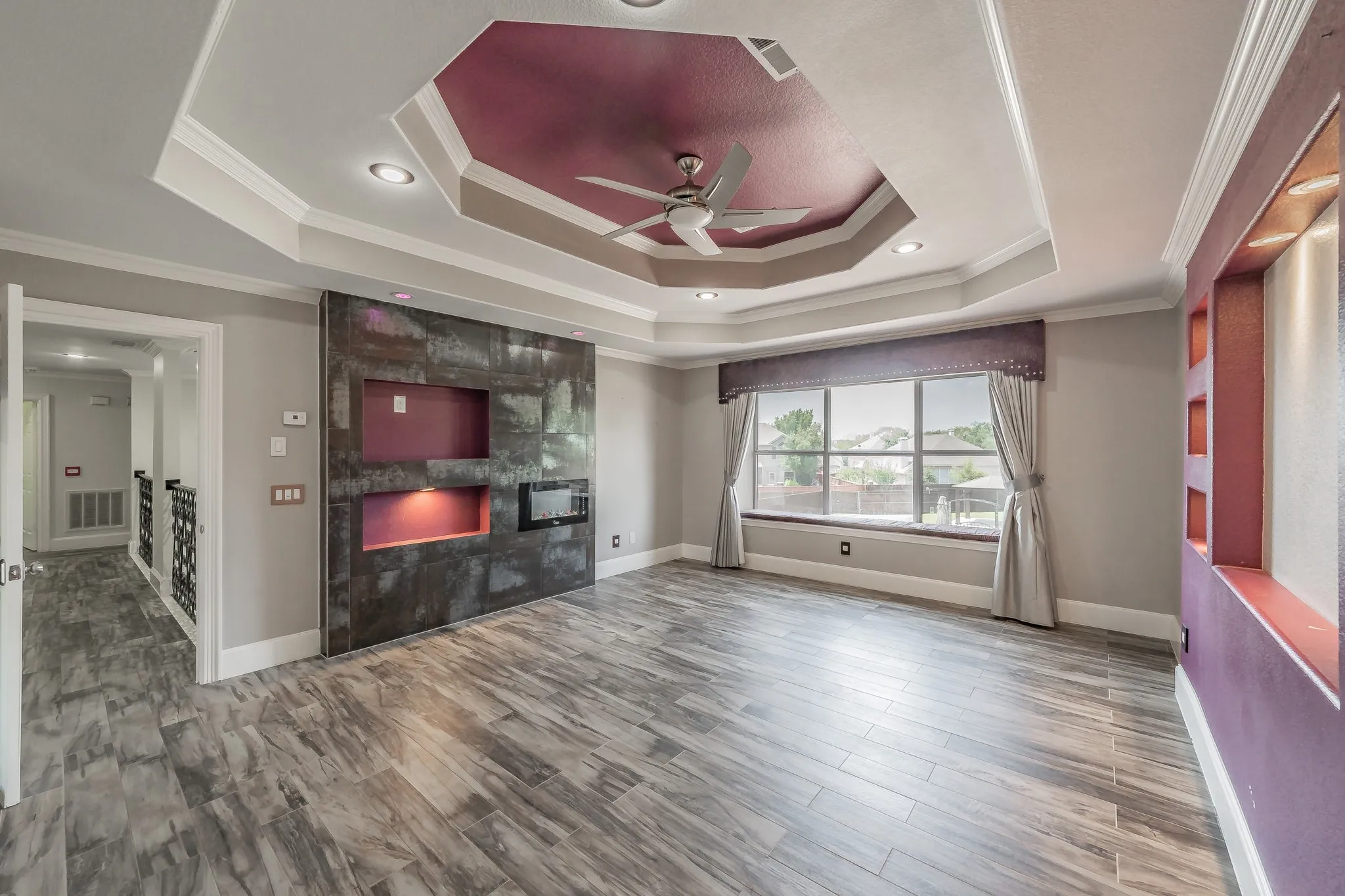 Tray ceiling with recessed lighting and a ceiling fan, custom media wall with built-in fireplace.