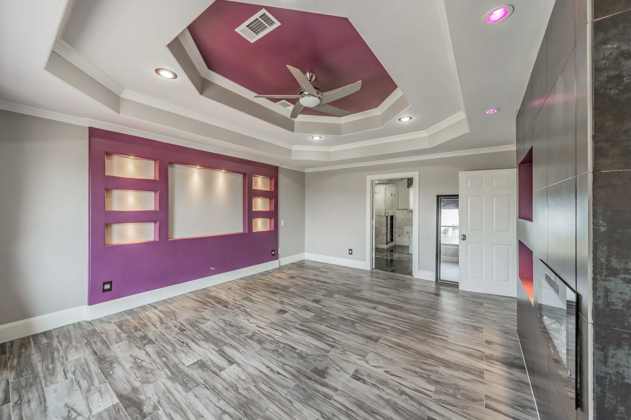 Tray ceiling with a ceiling fan, recessed lighting, built-in wall niches, and a built-in electric fireplace.