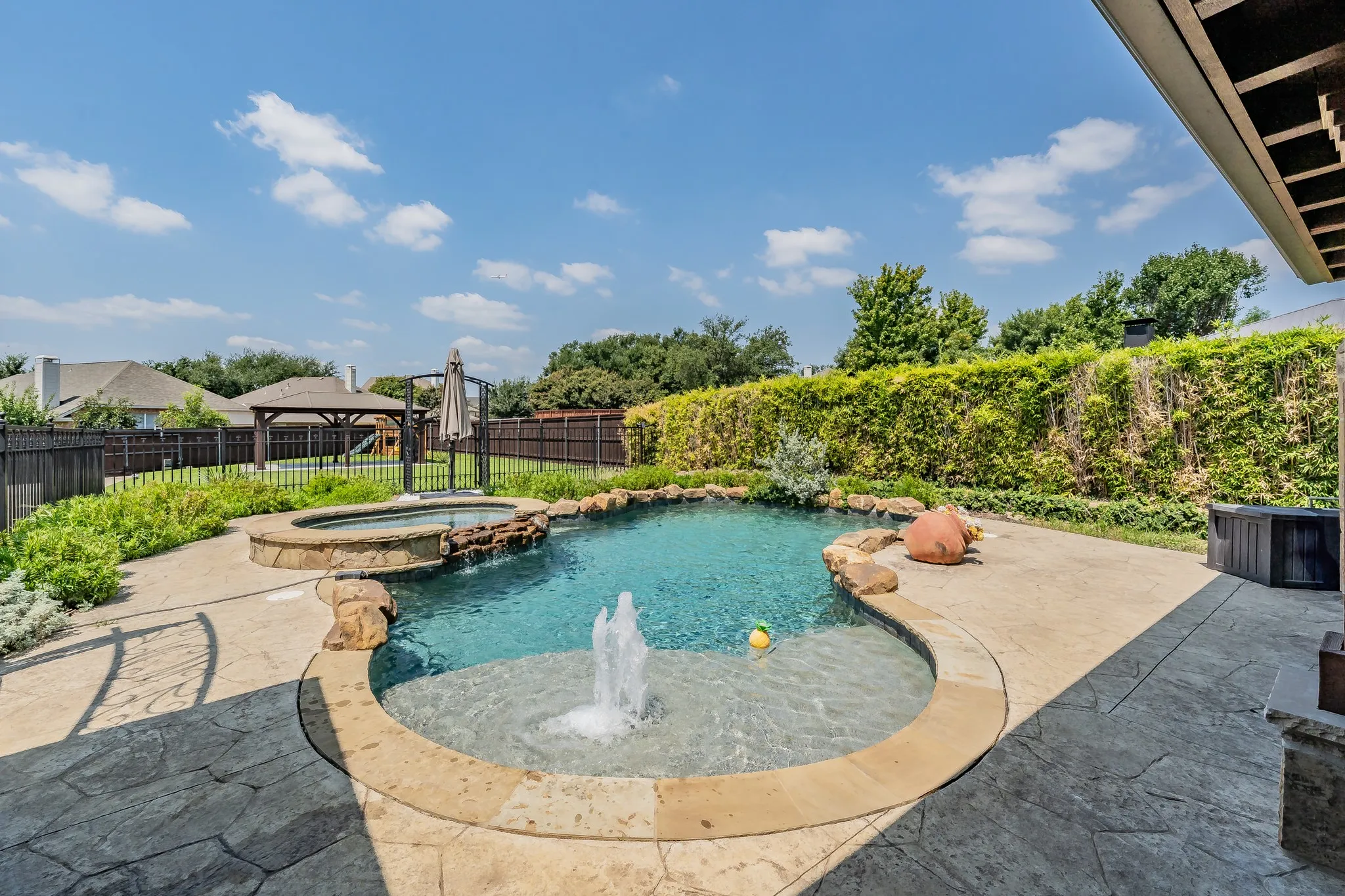 Backyard oasis with swimming pool, hot tub, gazebo, playset, outdoor kitchen fireplace, & covered patio.