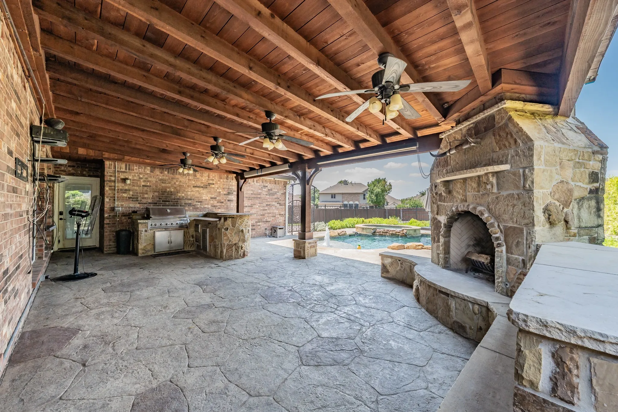 Expansive covered patio featuring an exposed wood beam ceiling and multiple ceiling fans