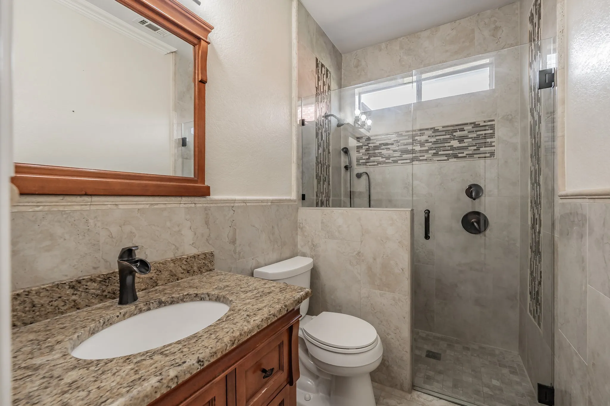 Tiled vanity with a granite countertop, undermount sink, and walk in shower.