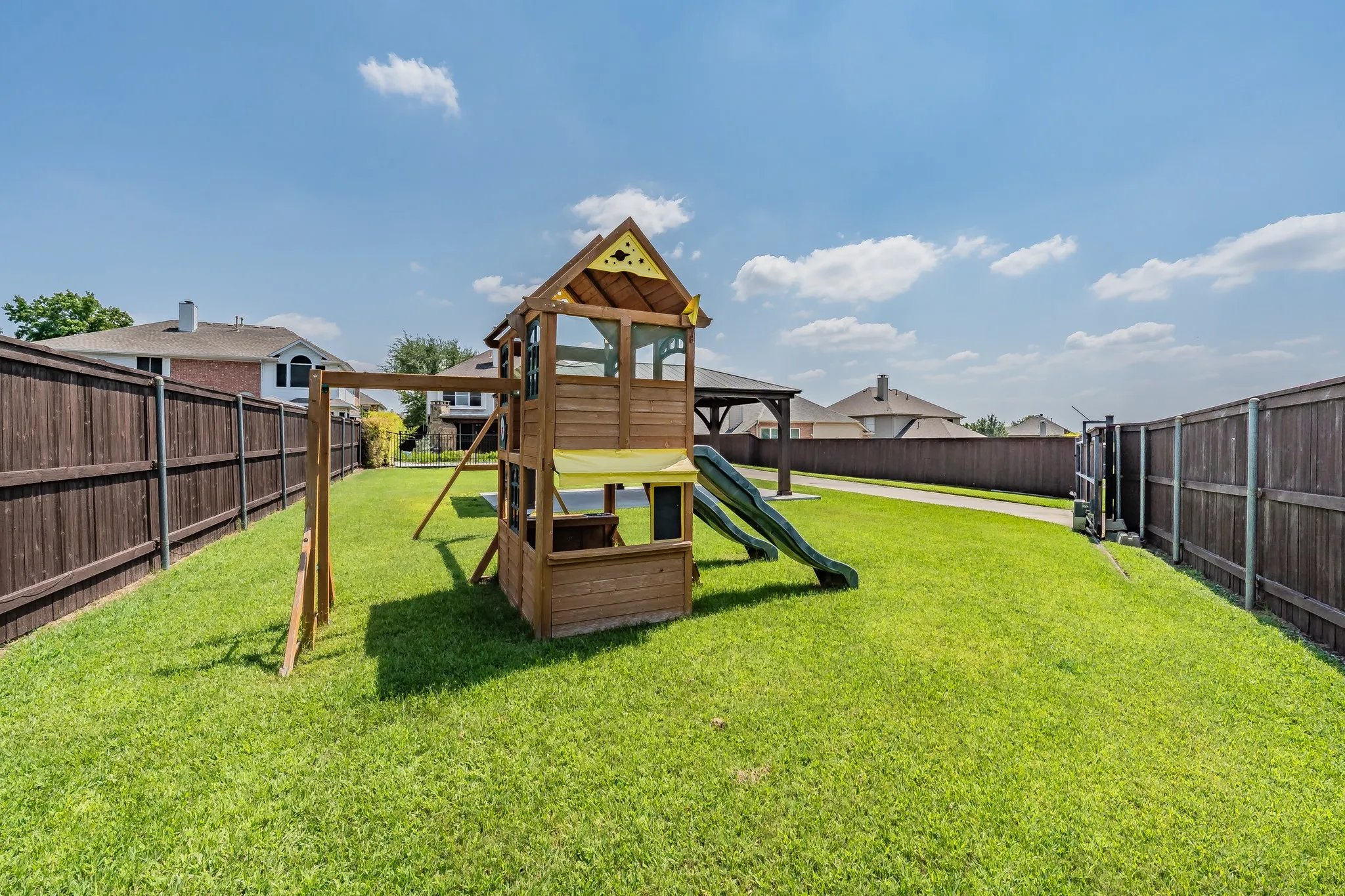 Large yard with a wooden privacy fence, swing set, and playset