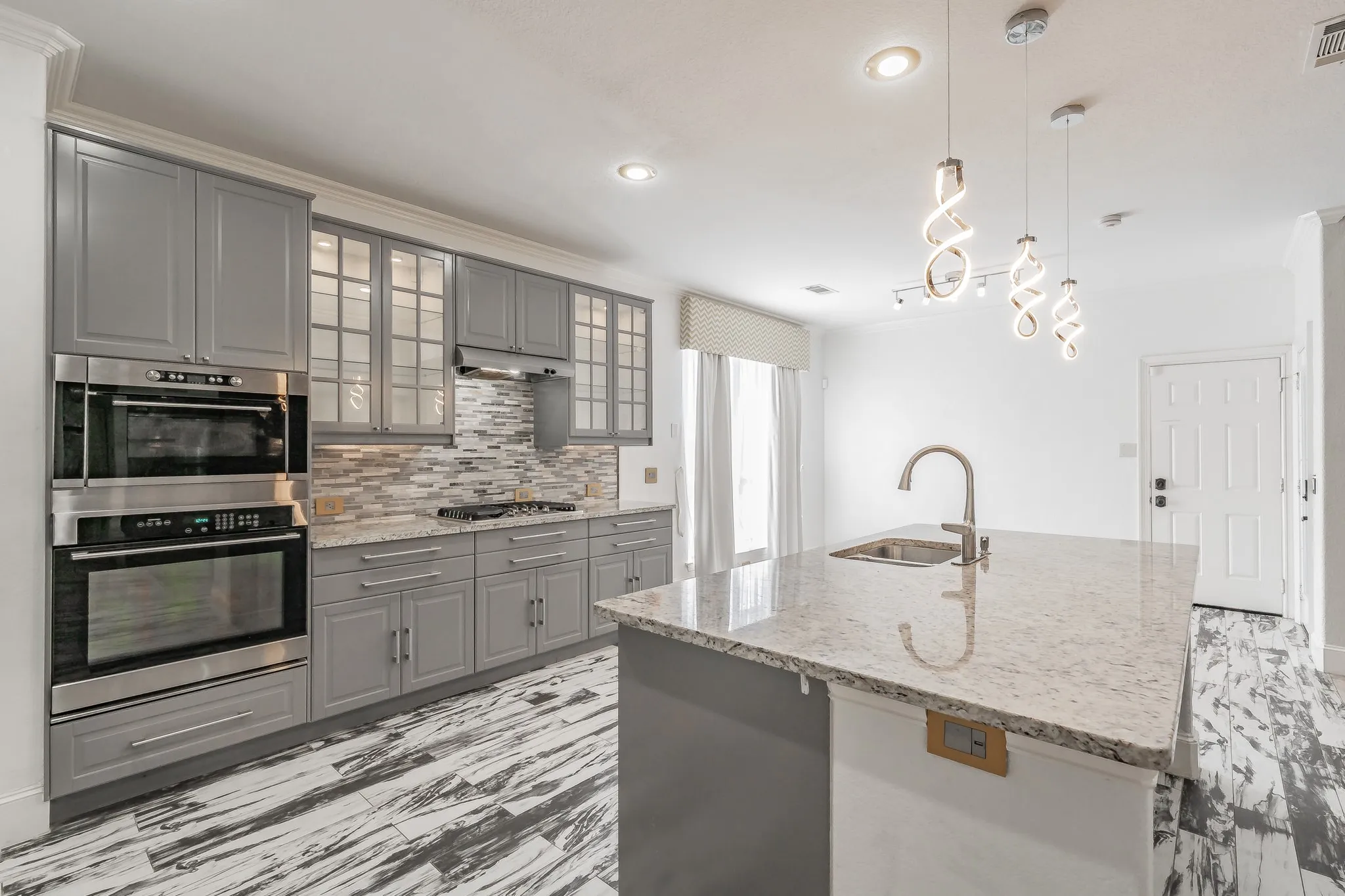 Kitchen featuring stainless steel appliances, grey cabinetry, a tile backsplash, and an island with an integrated sink