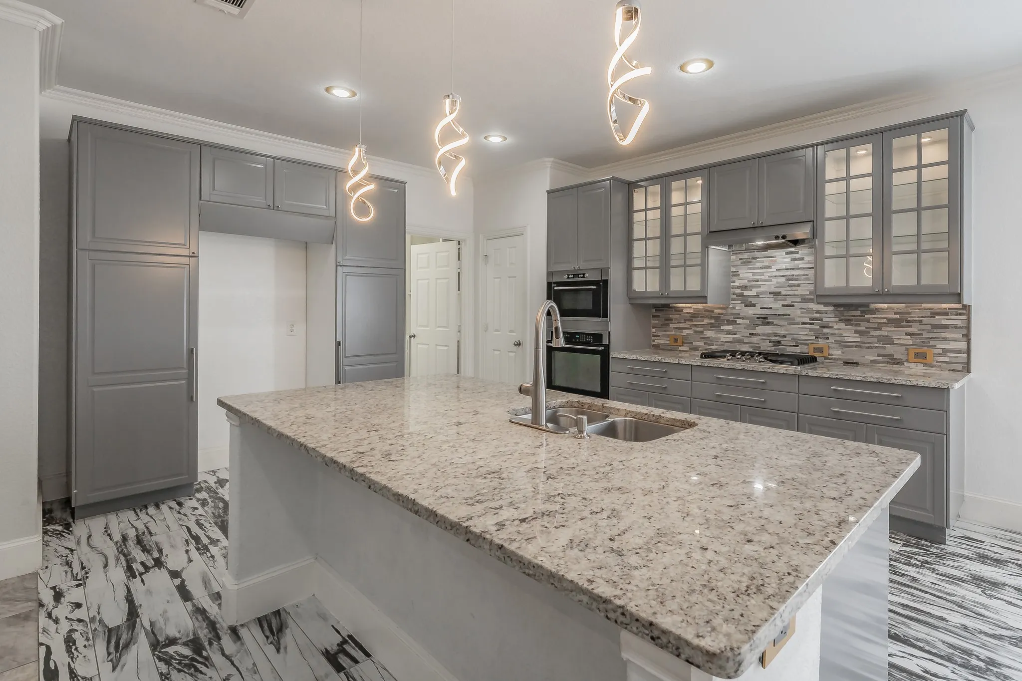 Spacious kitchen featuring a large island with an undermount sink, grey cabinetry, stainless steel appliances, a mosaic tile backsplash, and decorative pendant lighting