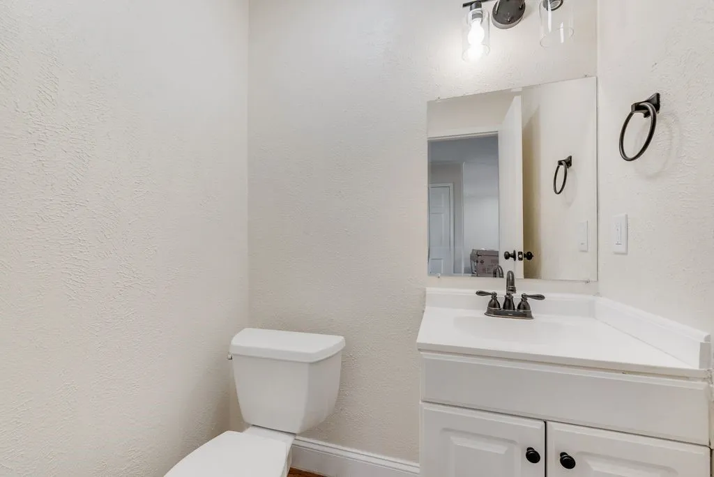 Bathroom featuring a white toilet, single-sink vanity with white cabinetry, wall-mounted mirror, and overhead lighting