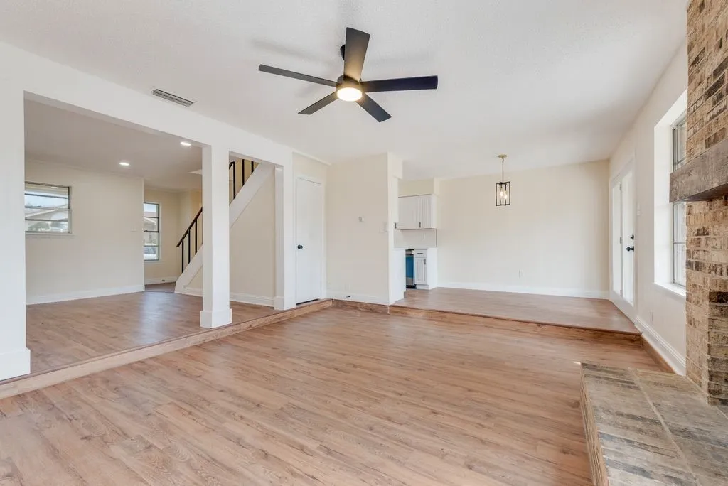 Wood-finish flooring throughout, with a recessed area featuring a fireplace with a brick surround and wood mantle