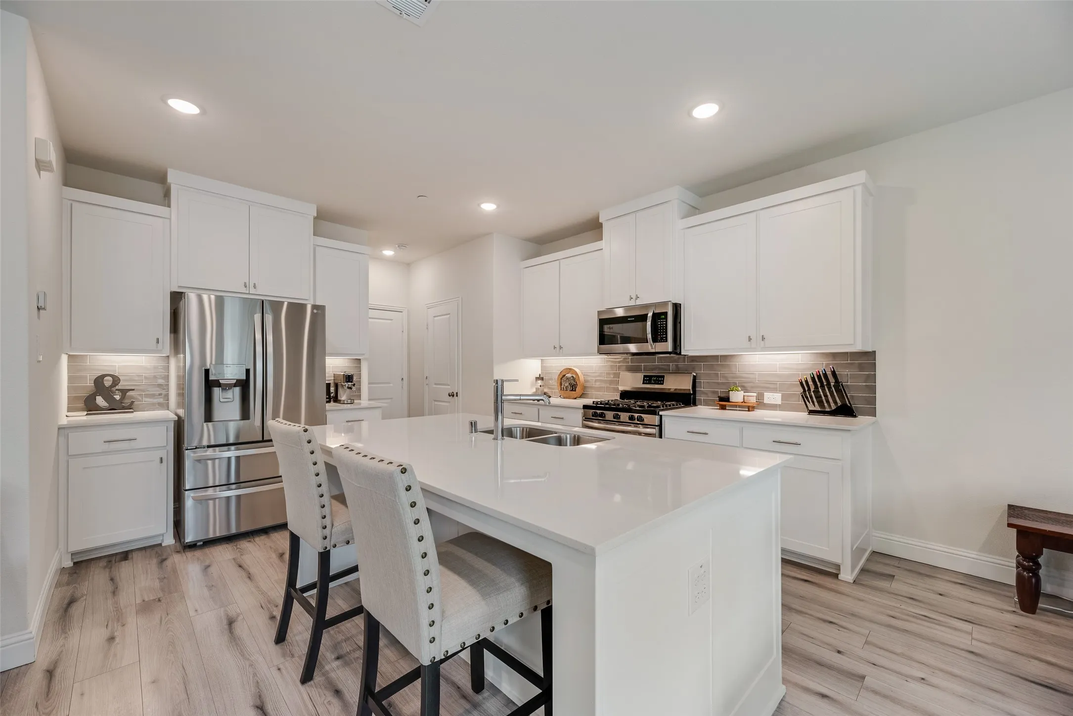 Modern kitchen featuring white cabinetry, a large kitchen island with counter seating, stainless steel appliances, wood-finish flooring, and recessed lighting
