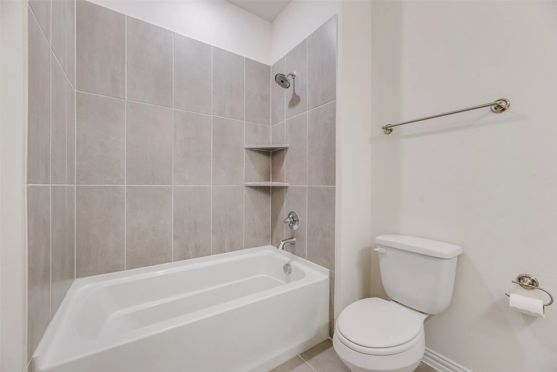 Bathtub and shower combination featuring neutral-toned tile surround, built-in shelving, and a chrome shower head with matching fixtures