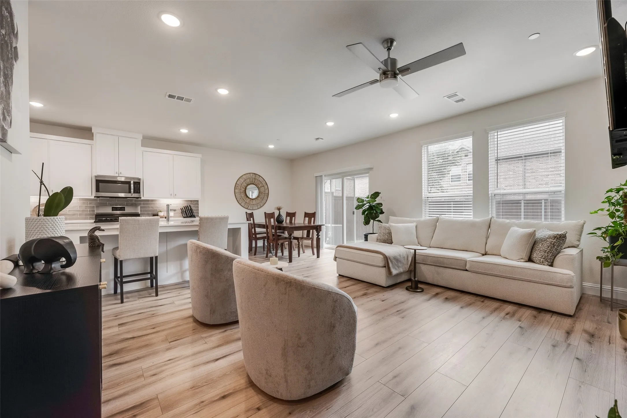 Open-concept living space featuring wood-finish flooring, recessed lighting, a modern ceiling fan, and white kitchen cabinetry with stainless steel appliances