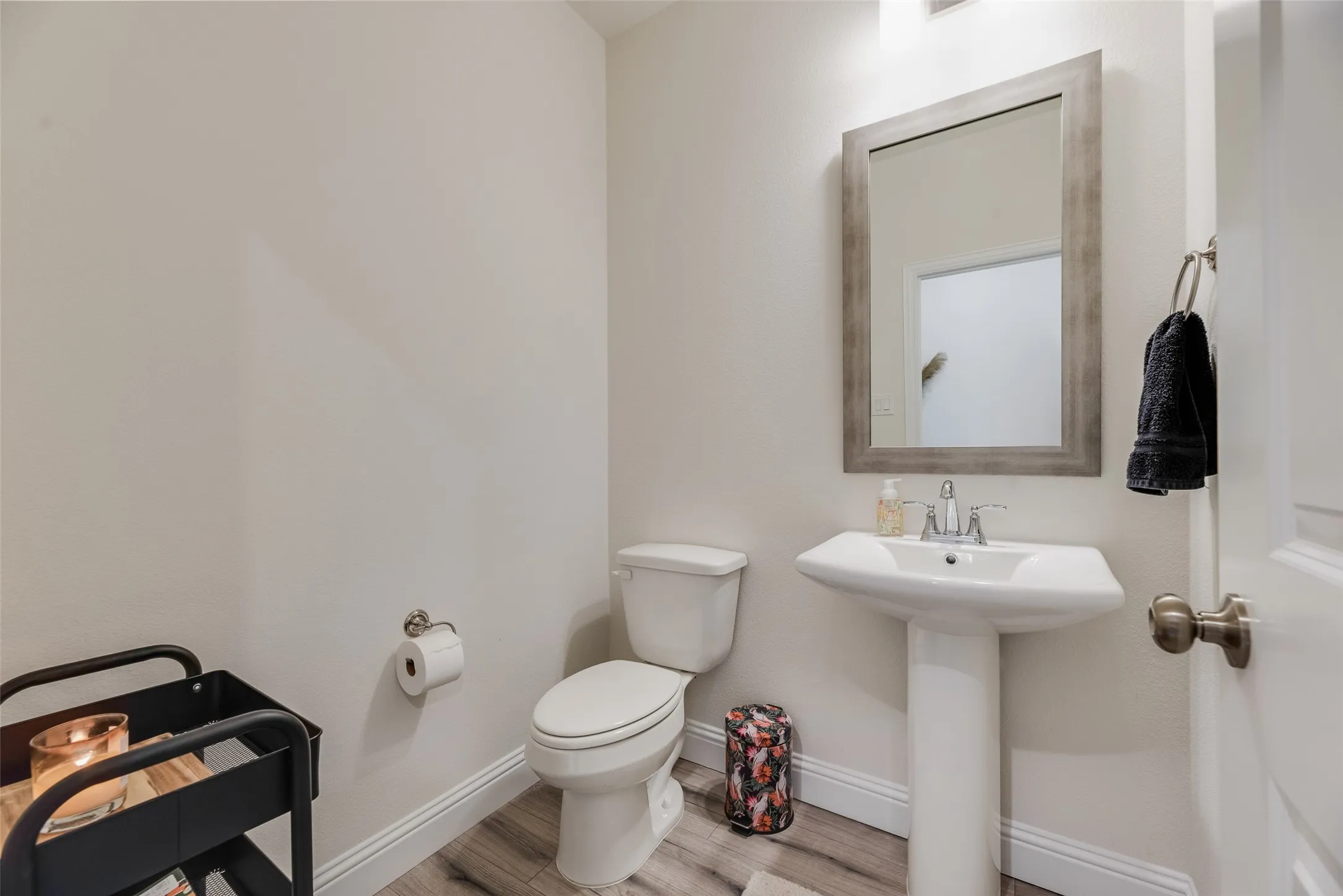 Pedestal sink with chrome fixtures, framed mirror, and wood-finish flooring