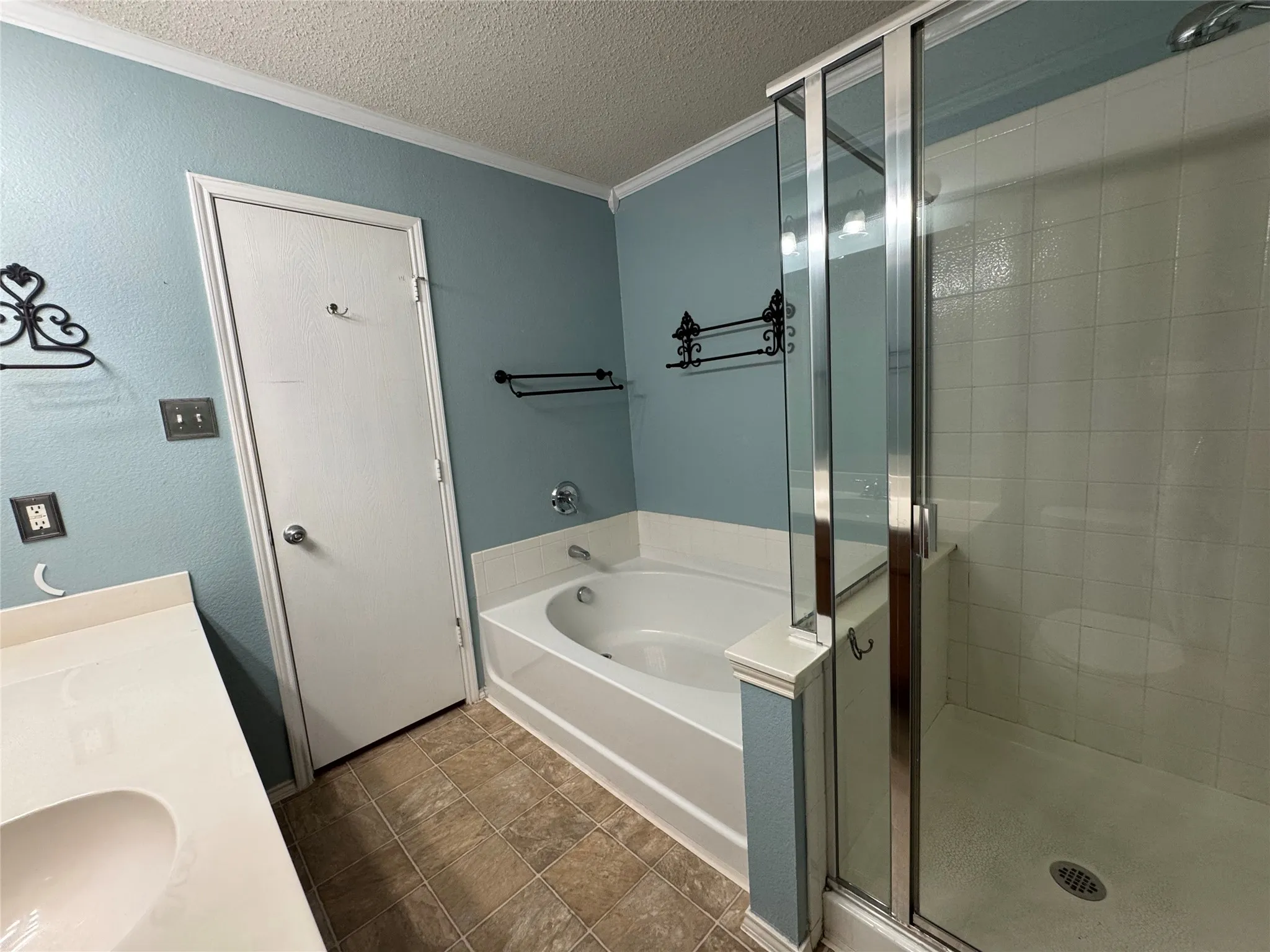 Built-in bathtub, glass-enclosed shower, single vanity with integrated sink, tile flooring, and crown molding