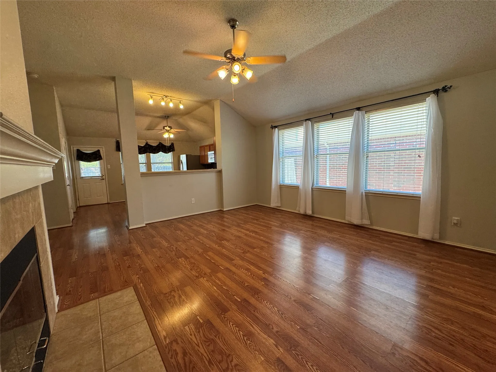 Vaulted ceiling with ceiling fan, wood-finish flooring, and multiple windows