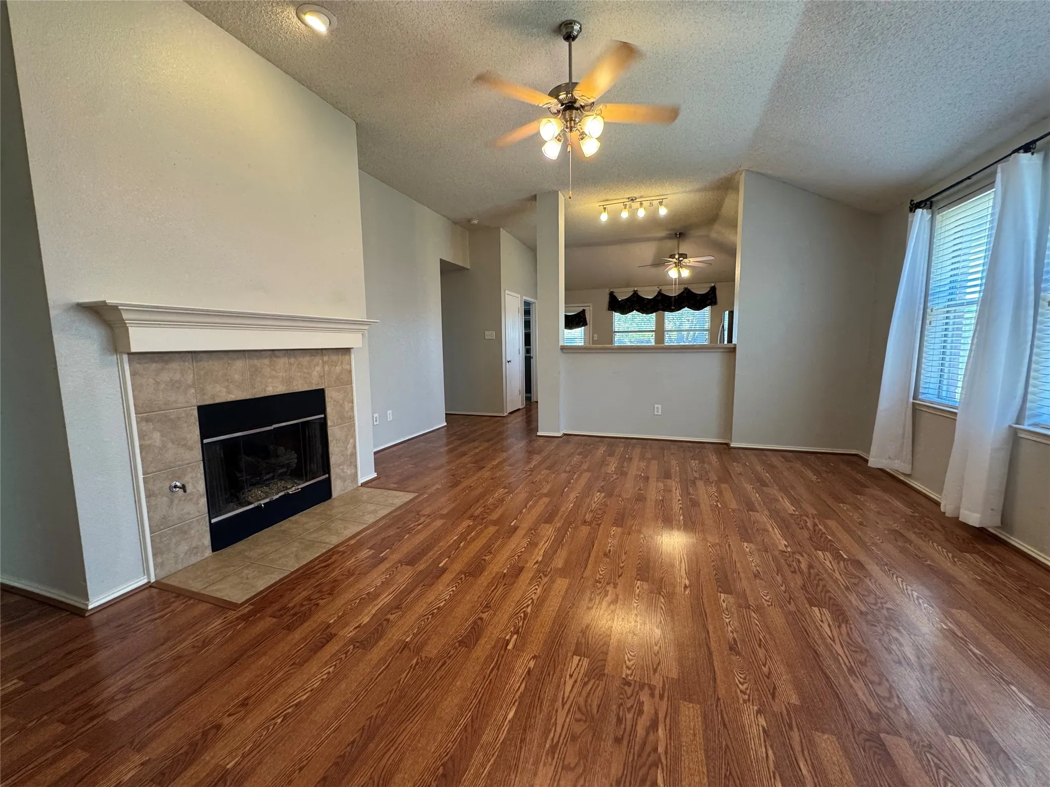 Wood-finish flooring, tiled fireplace with mantel, ceiling fan with integrated lighting, recessed lighting, and sloped ceiling