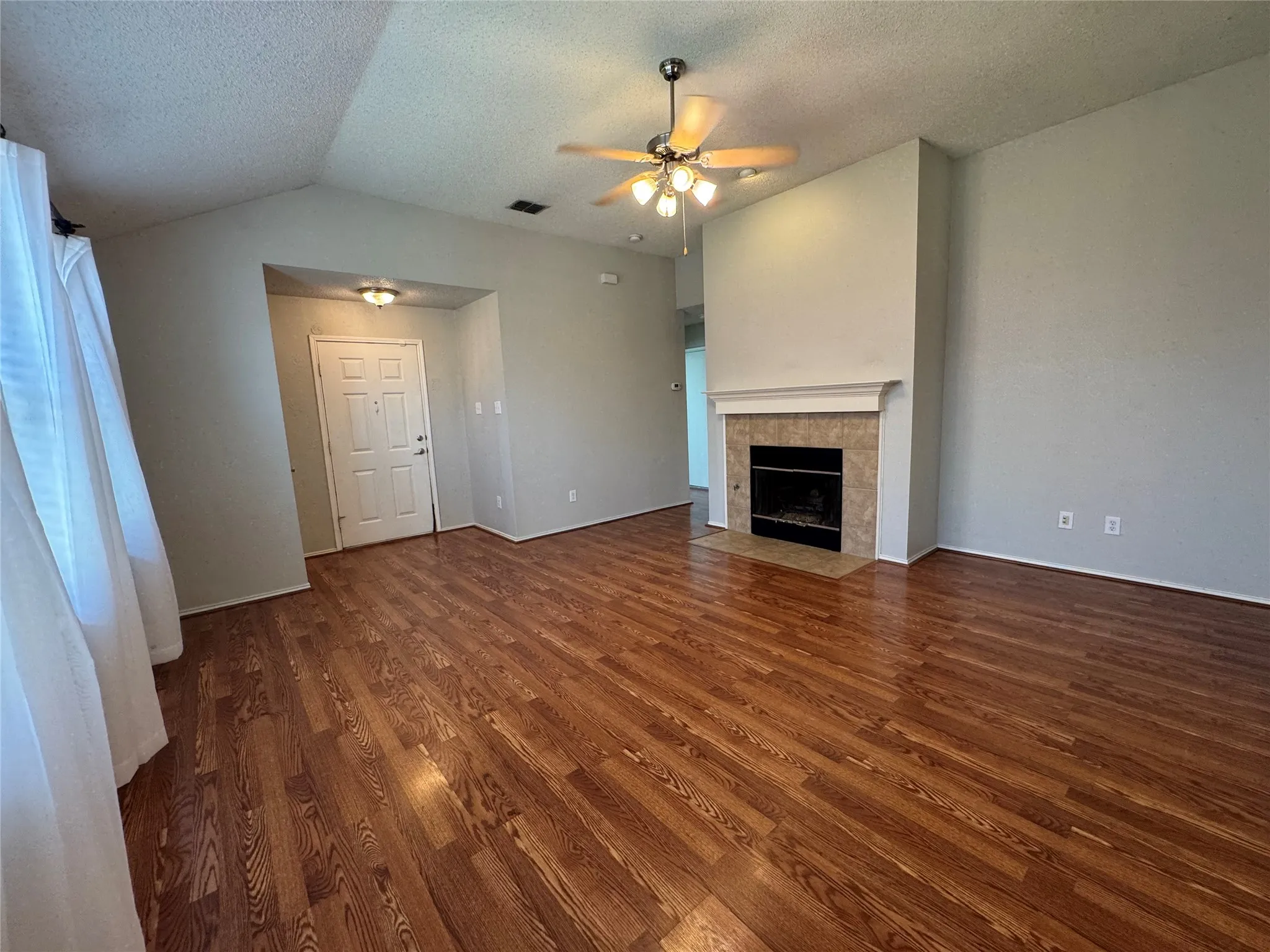 Vaulted ceiling with a ceiling fan, fireplace with a tile surround and mantel, wood-finish flooring, and a paneled entry door