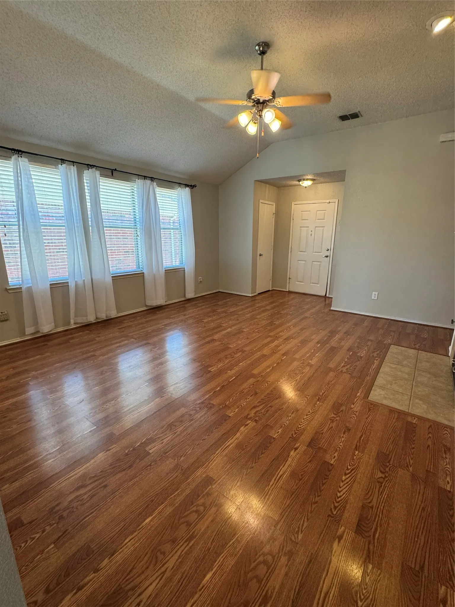 Vaulted ceiling with a ceiling fan light fixture, wood-finish flooring, multiple windows with blinds, and a paneled entry door
