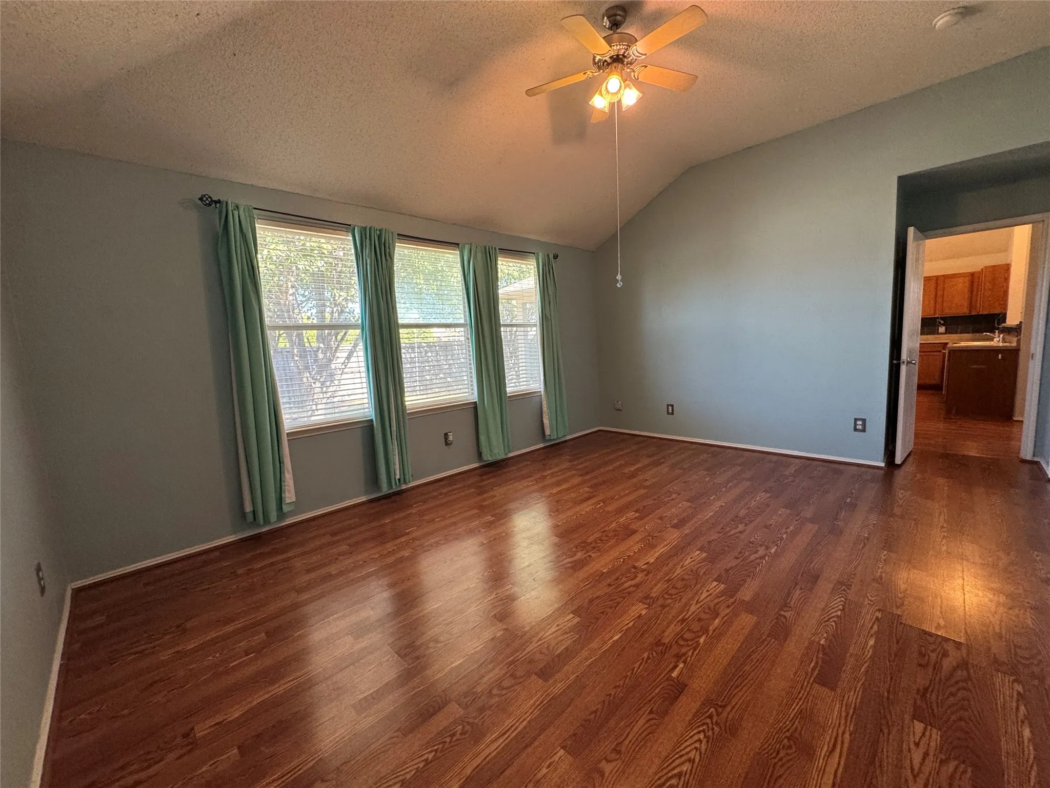 Vaulted ceiling with a ceiling fan, wood-finish flooring, and multiple windows