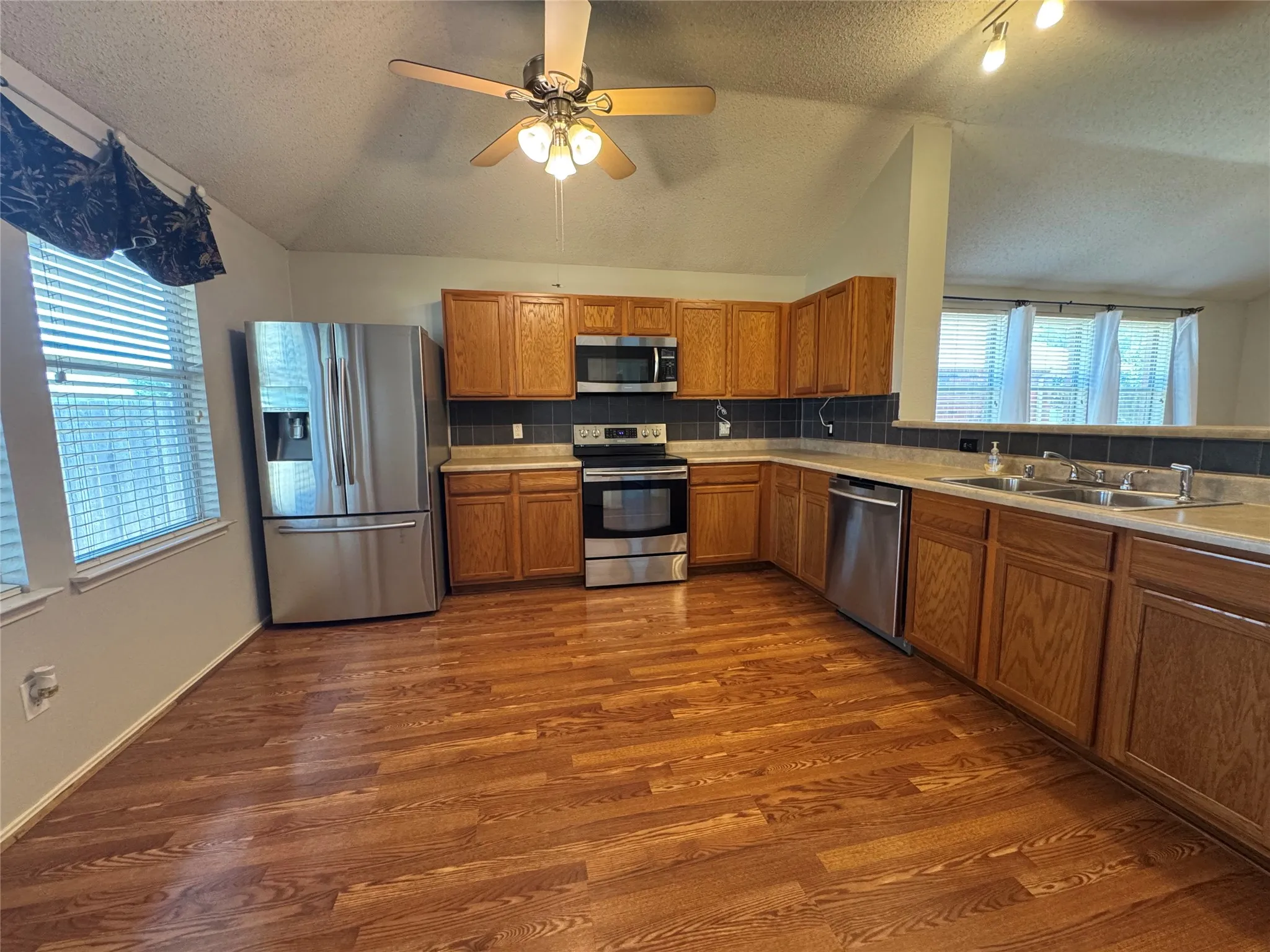 Kitchen featuring wood-finish flooring, wood cabinetry, stainless steel appliances, and a double basin sink