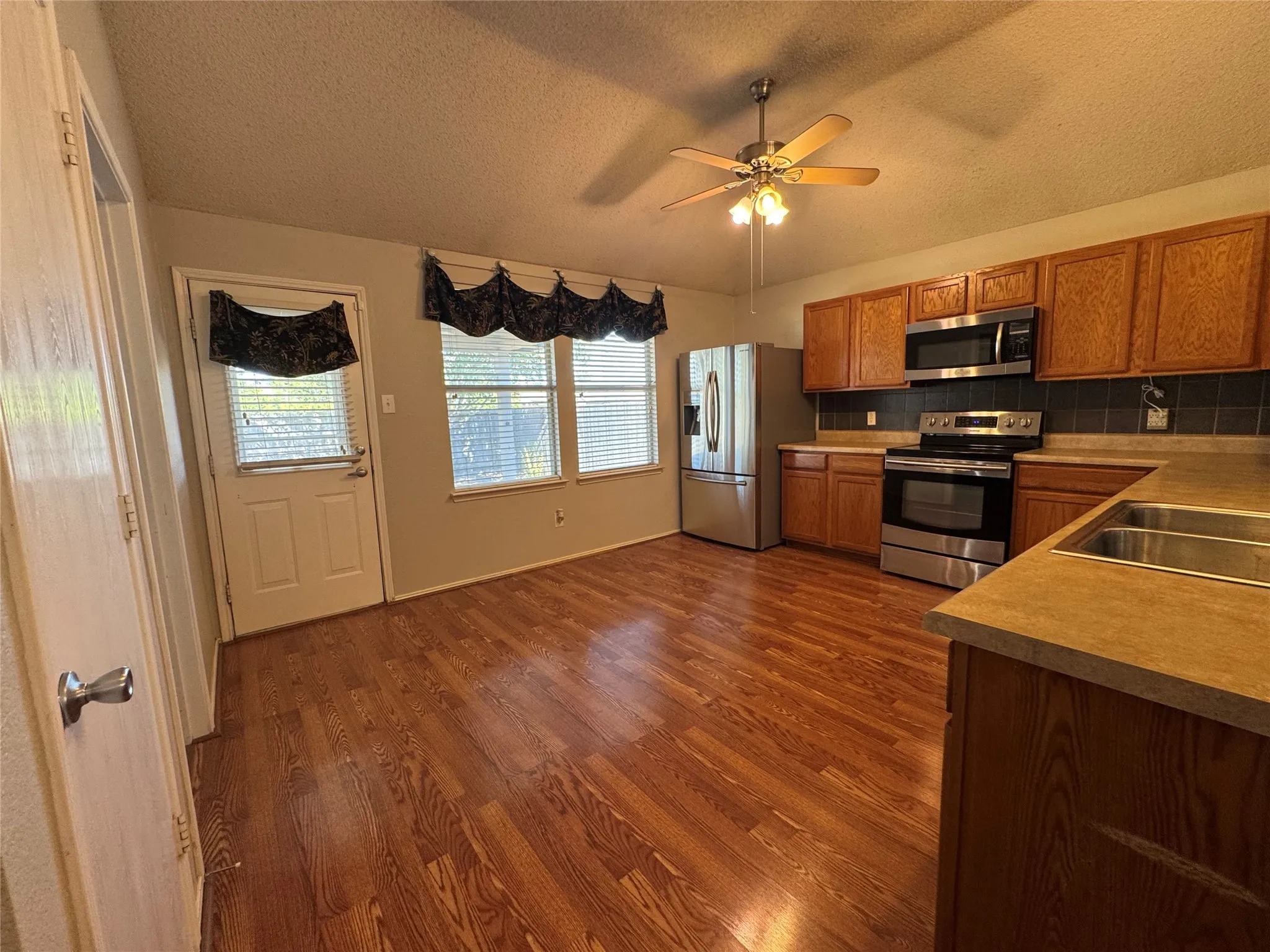 Wood-finish flooring, stainless steel appliances, wood cabinetry, built-in double basin sink, and a ceiling fan with integrated lighting