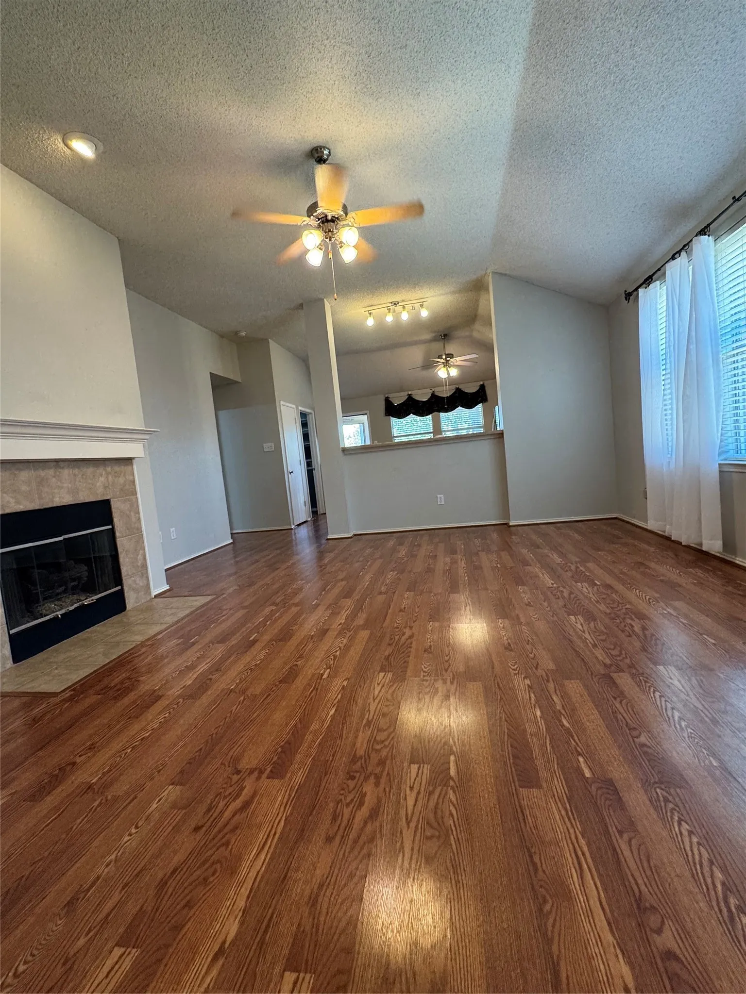 Vaulted ceiling with a ceiling fan, recessed lighting, wood-finish flooring, and a fireplace with a tile hearth