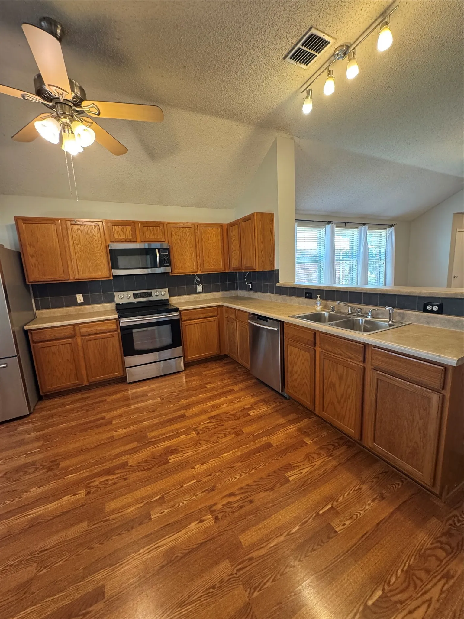 Kitchen featuring wood-finish flooring, wood cabinetry, stainless steel appliances, and track lighting